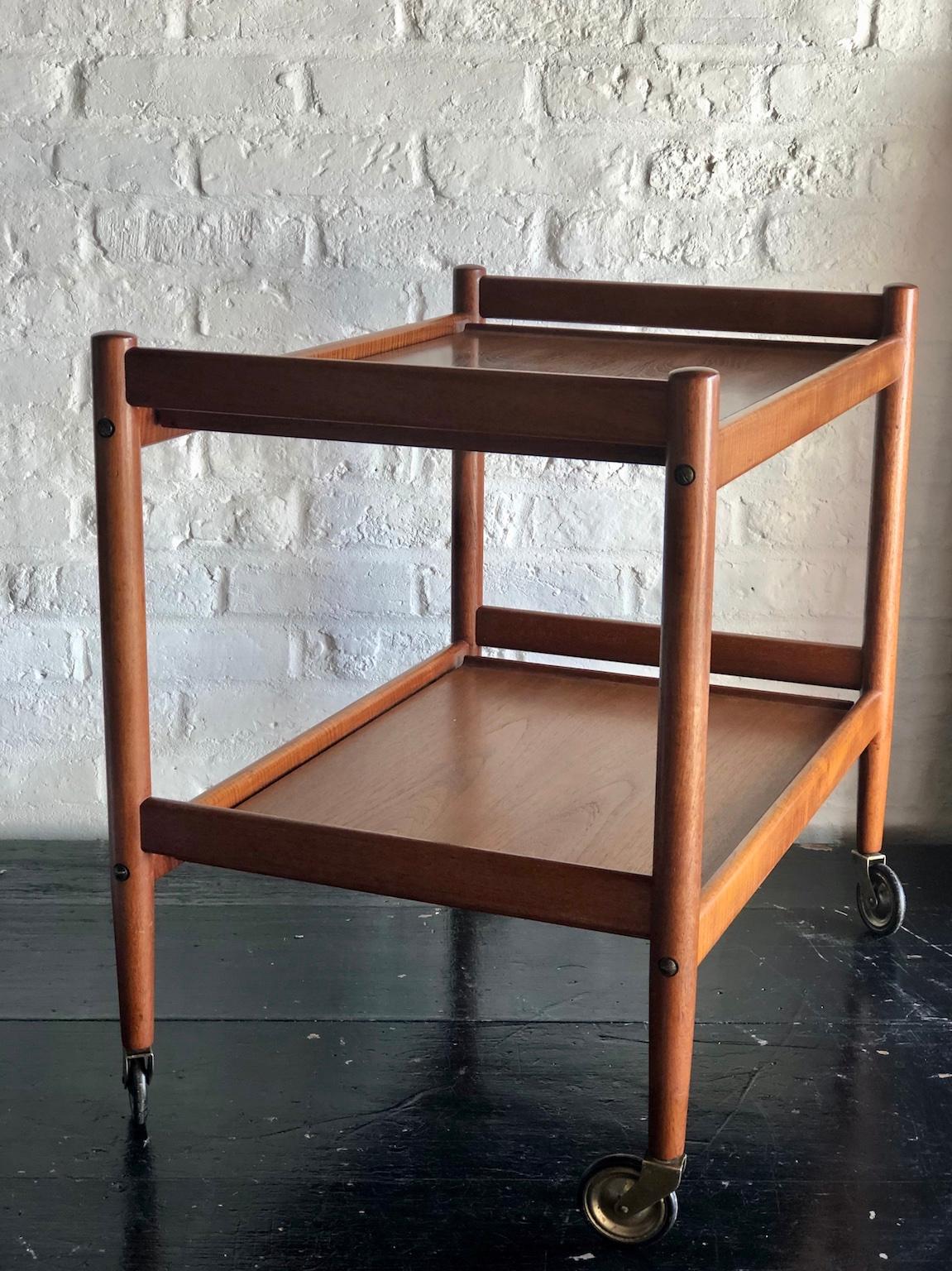 Mid century Danish teak drinks trolley / bar cart, 1960s

A two tier Danish teak trolley / bar cart with large rubber rimmed brass wheels.

Beautiful Danish quality and design, the shelf appears to be floating, but it is connected to 
the main