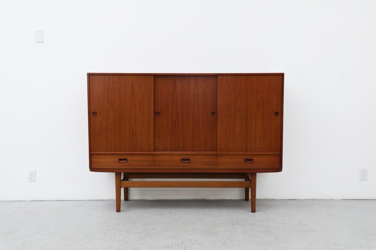 Mid-Century Modern Danish teak highboard with upper sliding door cabinets, green felt lined drawers and lower storage drawers. In good original condition with visible wear consistent with its age and use.