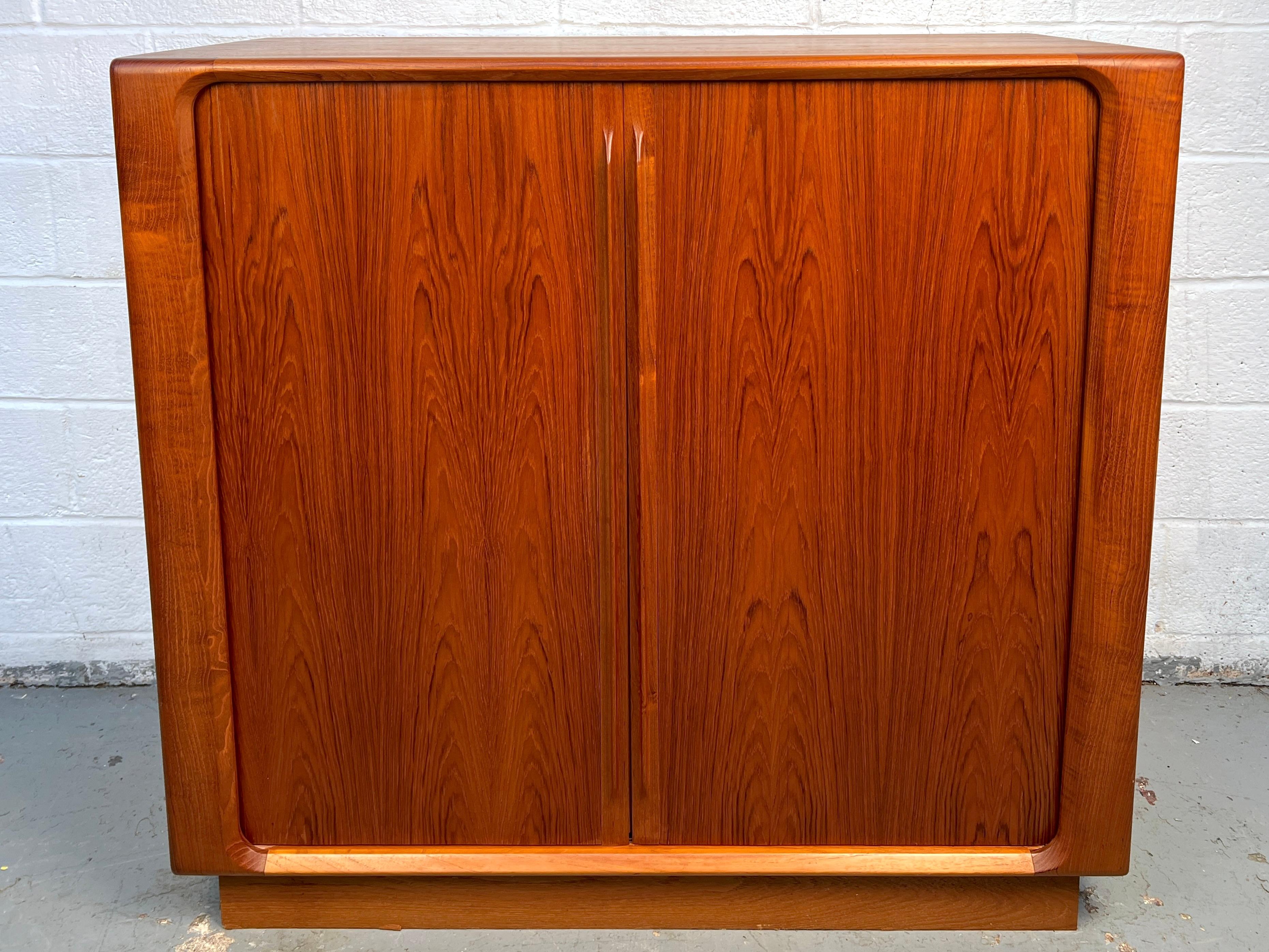 Un classico comò highboy danese della metà del secolo scorso, realizzato in caldo teak dall'azienda danese Bernh. Pedersen & Søn (BPS) della Danimarca. Presenta ante a tamburo lisce e ben funzionanti che rivelano un ampio spazio interno, oltre a