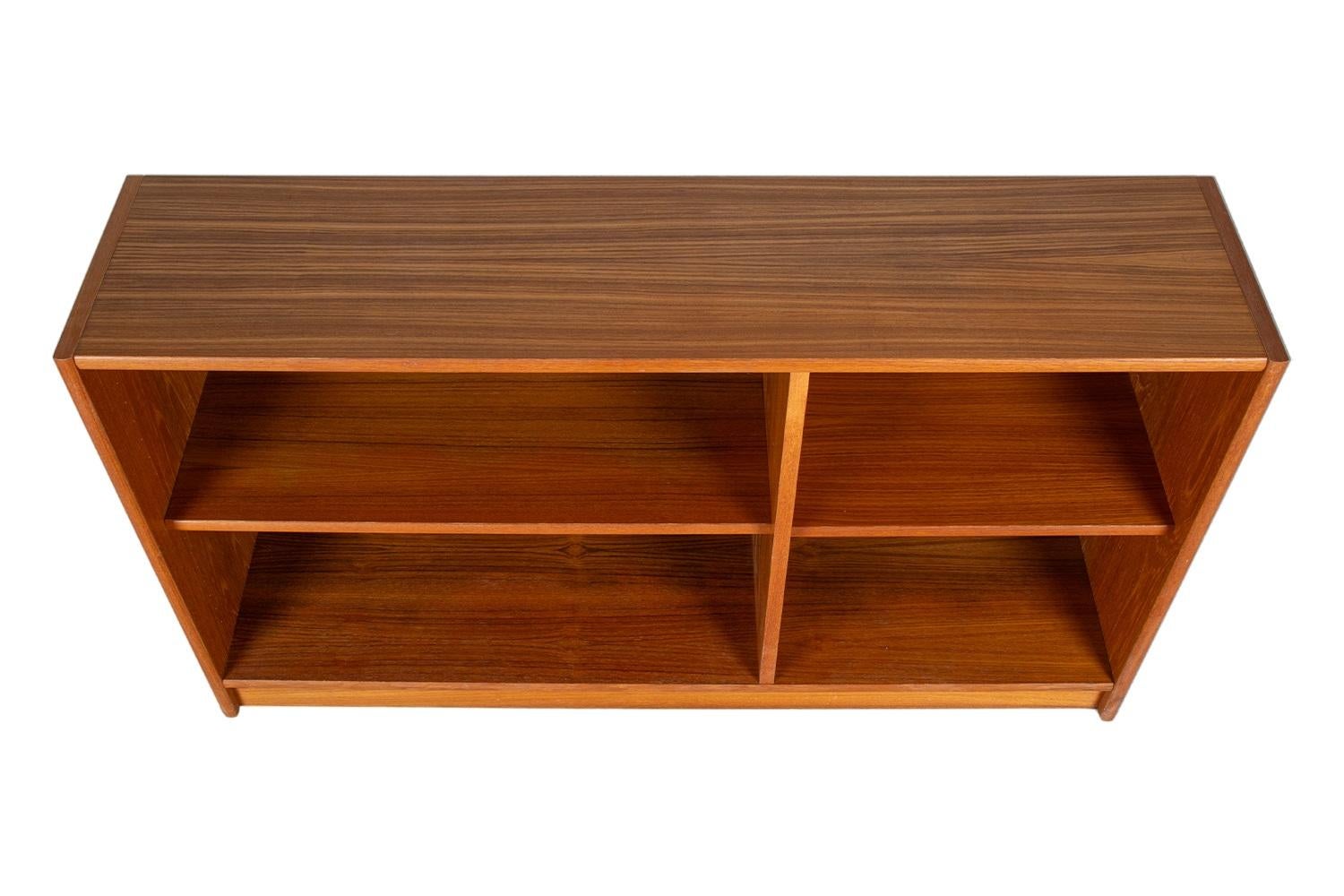 Fantastic Danish teak, low, compact bookcase made in Denmark. This slim beautiful vintage teak bookcase features two adjustable shelves, the left shelf measures 28″ wide x 11″ deep the right shelf measures 18″ wide x 11″ deep. The bookcase rests on