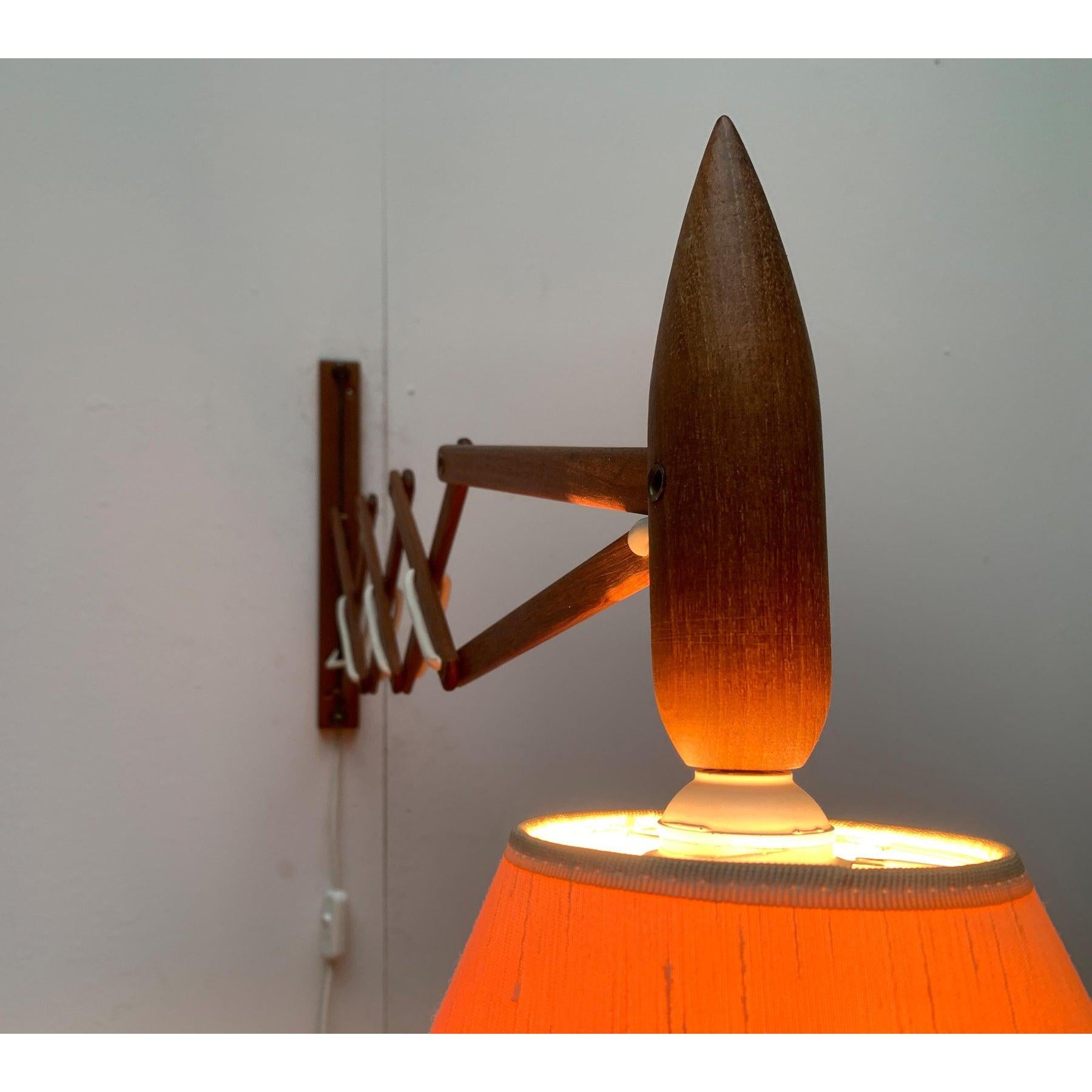 Lampada da parete con braccio flessibile a forbice del produttore danese Le Klint.

La lampada è composta da elementi in legno massiccio di teak. L'elemento in legno sulla cupola della lampada è progettato come una punta e funge da maniglia. Il