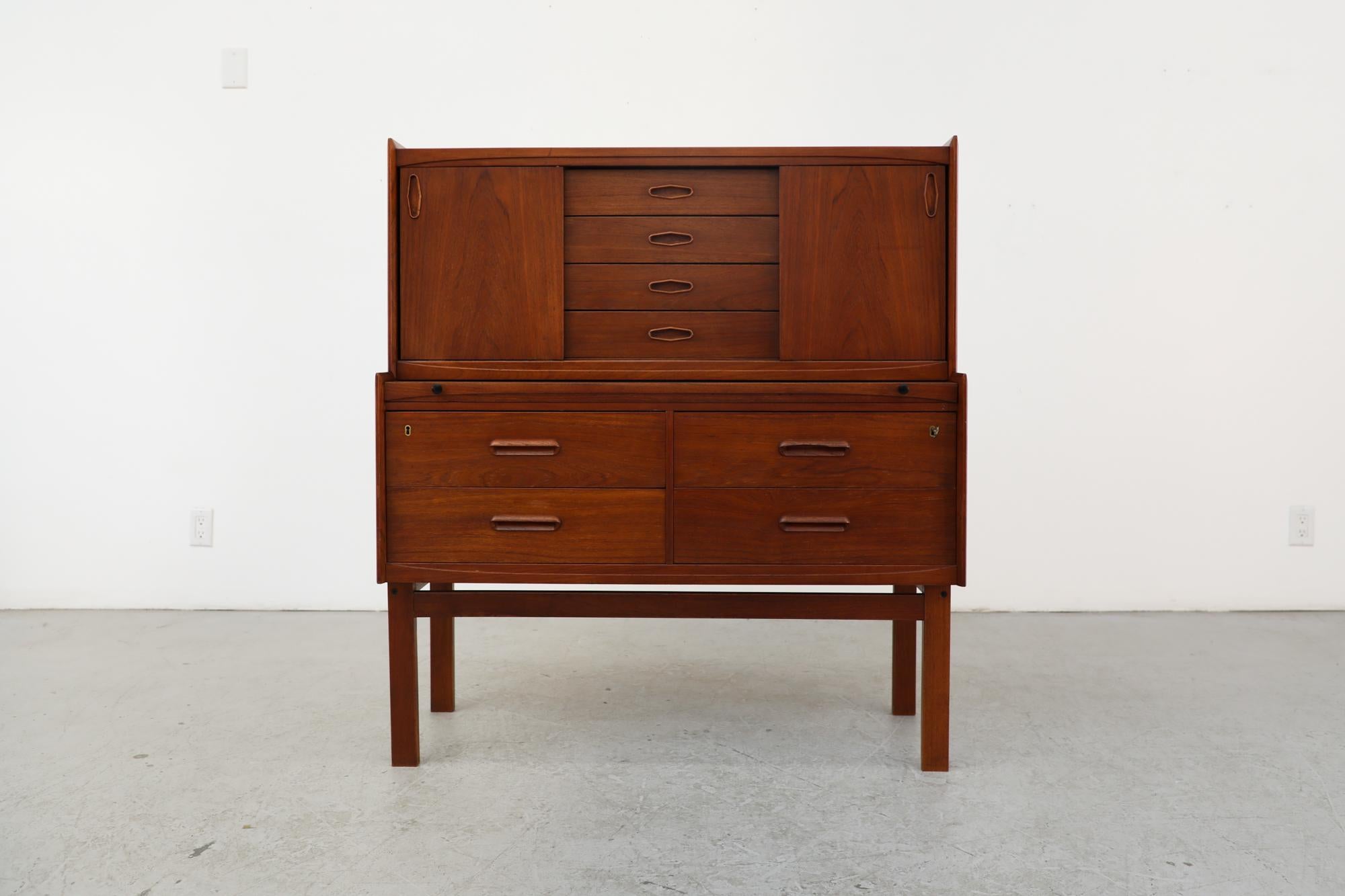 Mid-century Danish teak secretaire with hidden desk top, locking lower drawer and upper cabinets. Often used as a vanity, desk and/or dresser. The top portion has 2 sliding doors and 3 stacking drawers with organically carved inset handle pulls. The