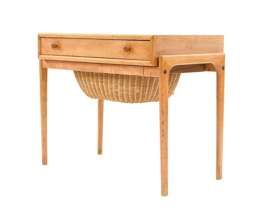 Mid-Century Modern teak sewing table in the style of Hans Wegner. Single upper drawer featuring small divided storage sections, as well as pull out / pull-out storage basket in great condition. The light teak shows some small signs of