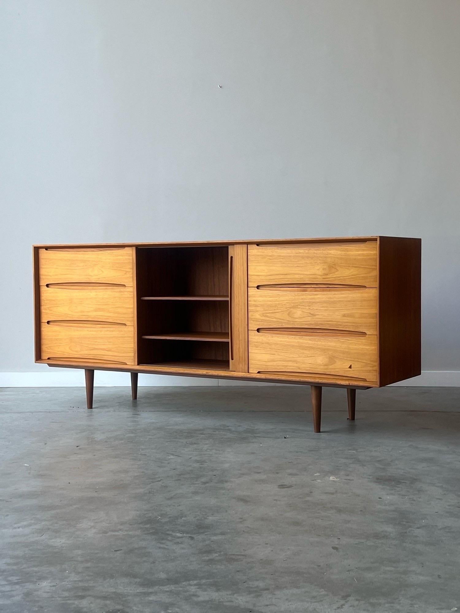 Precioso aparador de teca de mediados de siglo, de Dyrlund, Dinamarca. La puerta de persiana central da acceso a una estantería abierta ajustable, ideal para objetos, equipos de audio y multimedia, ¡o perfecta para discos! 3 cajones izquierdos y 3