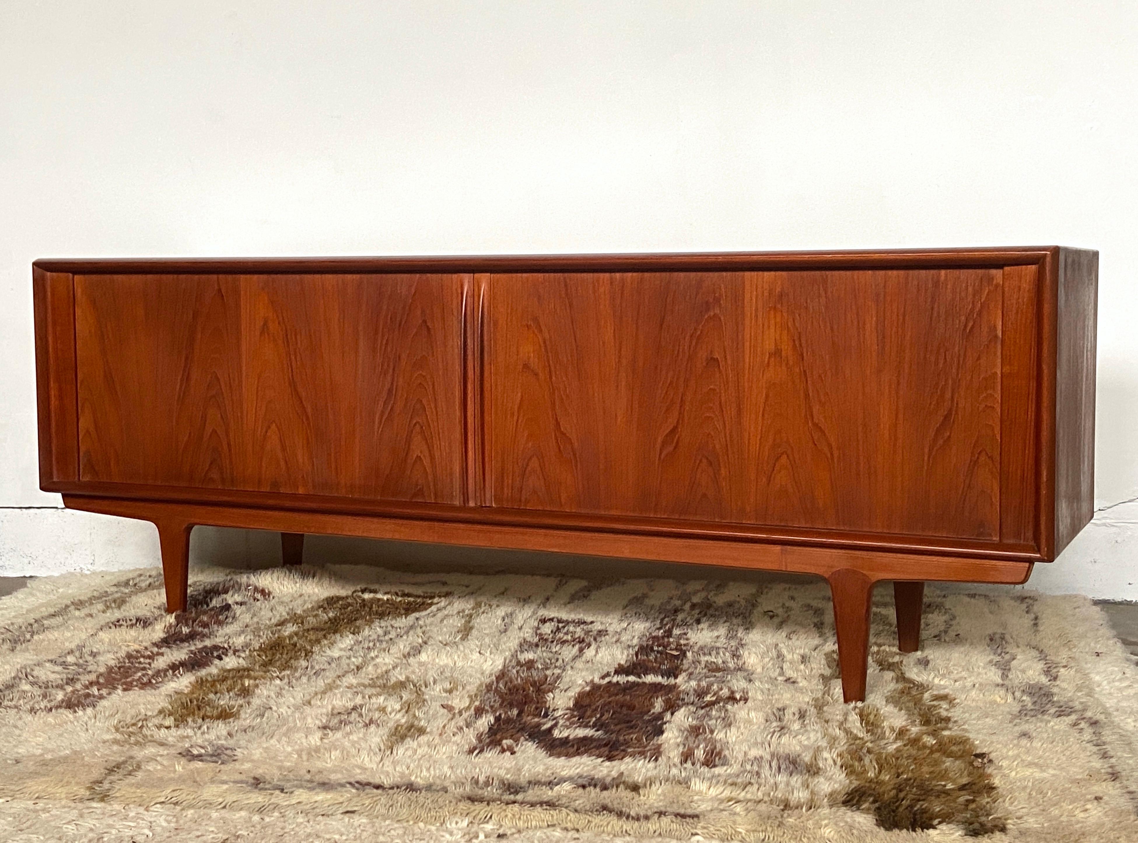 Splendida credenza in teak danese di metà secolo di Bernhard Pedersen - splendidamente realizzata con ante scorrevoli a tamburo, finiture scolpite, maniglie e gambe in teak vecchio di tonalità scura.
Condizioni vintage molto belle, la parte