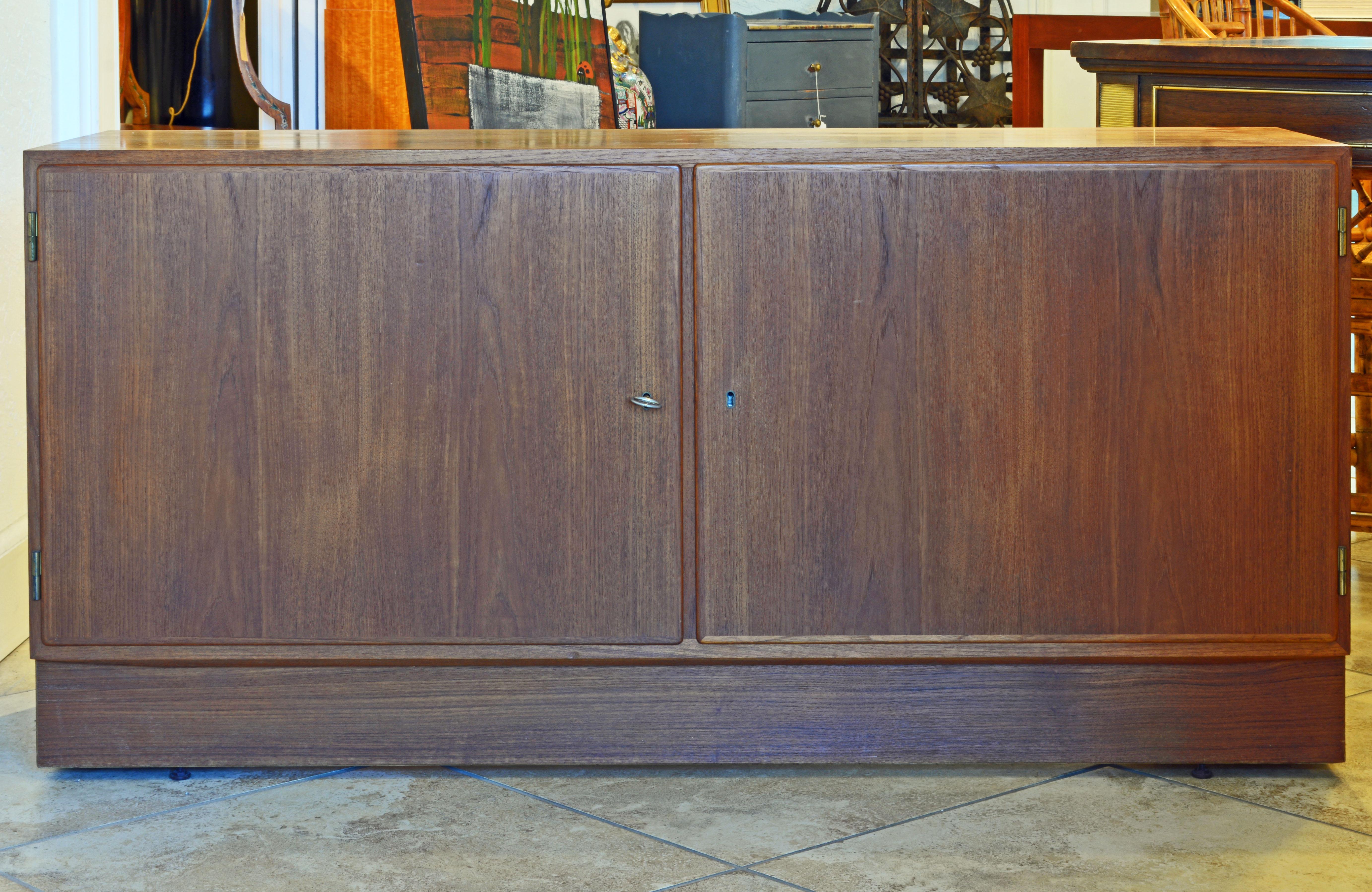 In a Classic Minimalist design this fine piece of furniture shows beautifully grained teak on the top, front and sides. The sideboard features two doors with locks opening up to an interior fitted with drawers and adjustable shelves. The Poul