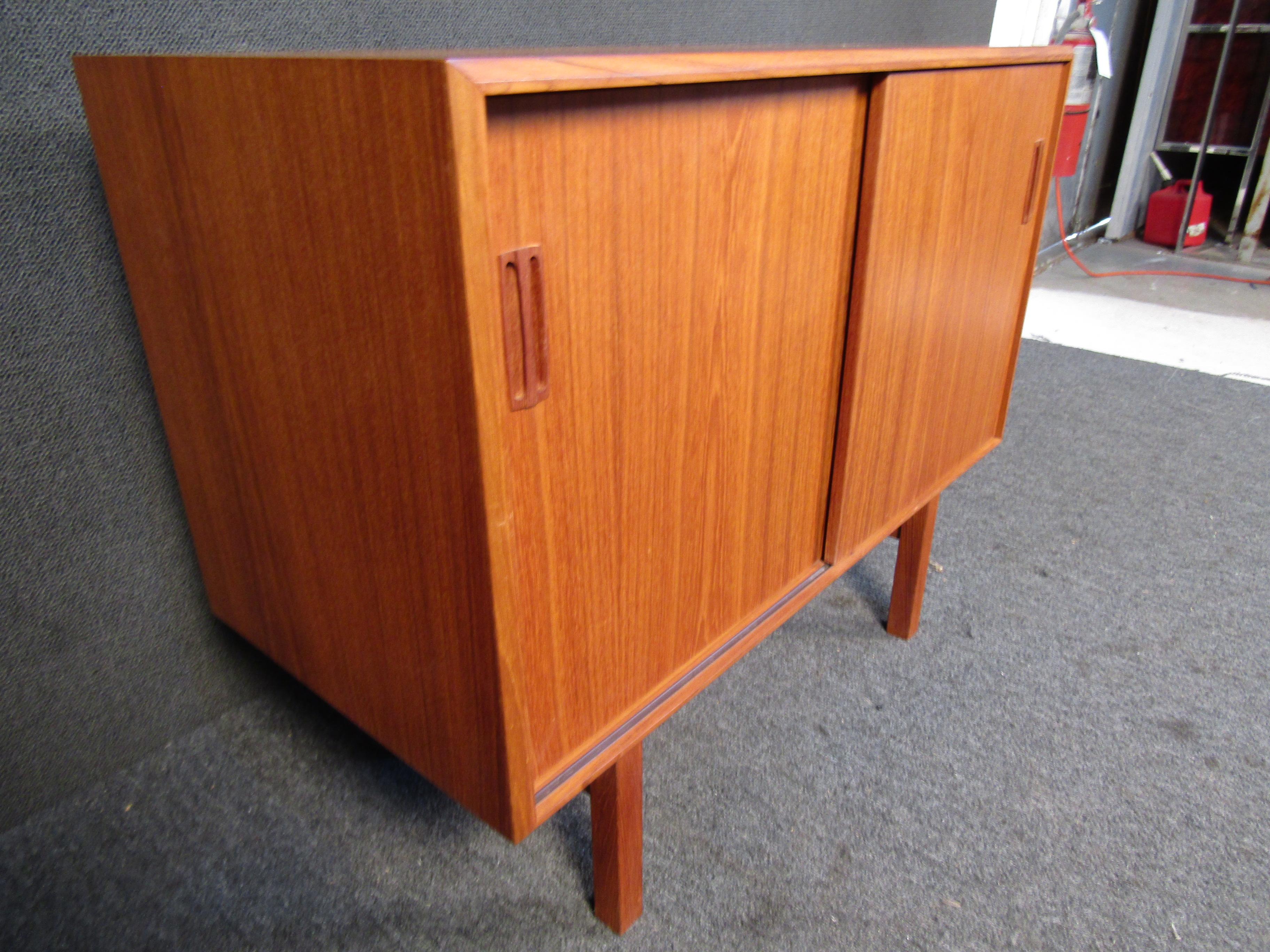 Rich teak wood is combined with an understated Mid-Century Modern design in this vintage Danish cabinet. Sliding doors reveal shelving and plenty of space for storage. Please confirm item location with seller (NY/NJ).