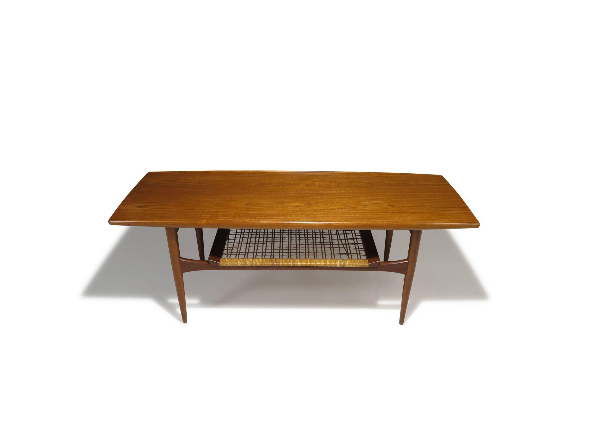 Beautifully crafted, this mid-century Danish teak coffee table features a sculptural raised-edge surface and a woven caned lower shelf Professionally restored with a hand-rubbed natural oil finish, the table is in excellent condition, showing only