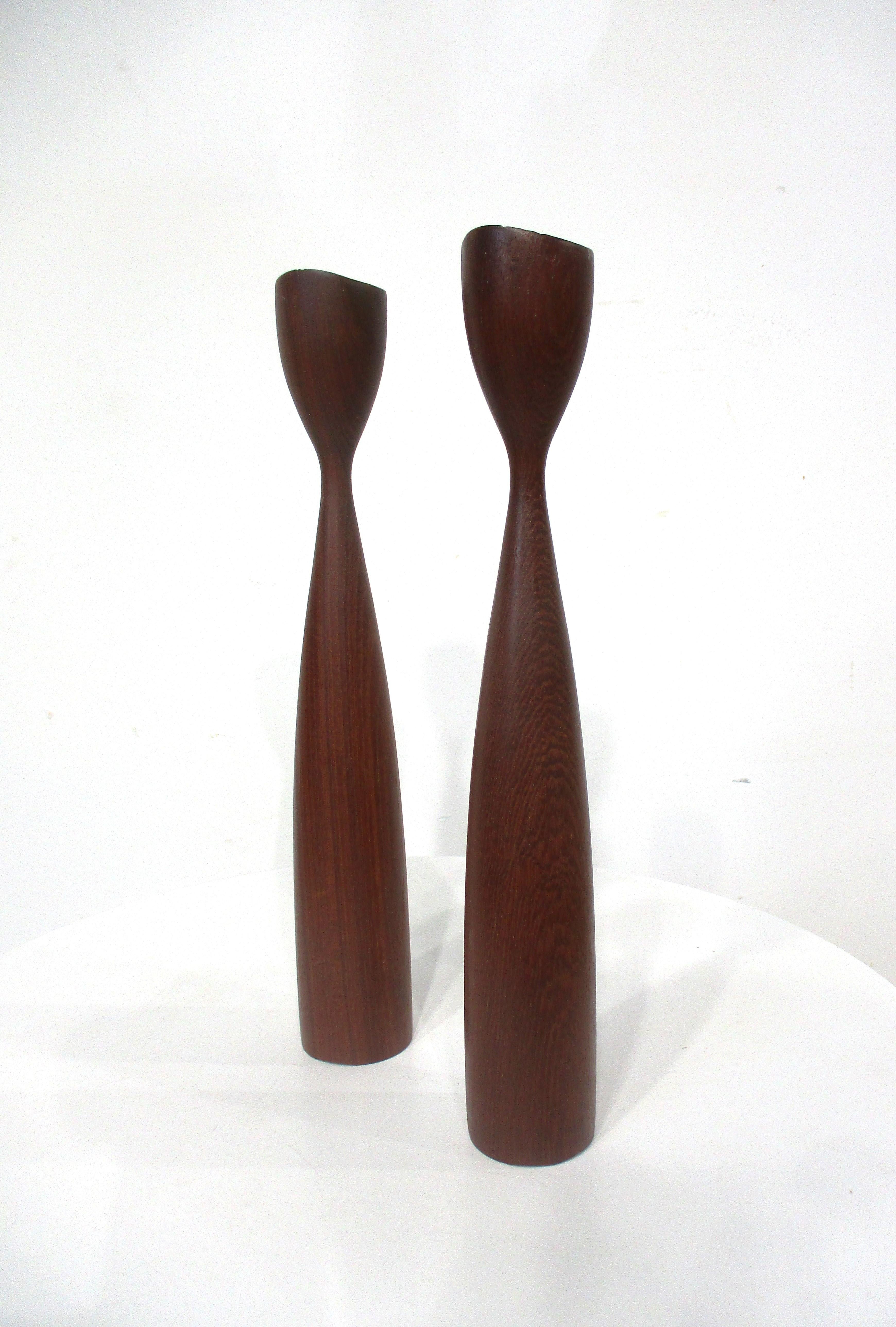 A pair of sculptural teak wood candlesticks with tall slender necks and heavy  weighted bases . Inside the candle area there are brass inserts for easy installing , removing and cleaning of the wax , retains the branded marks to the bottom of each