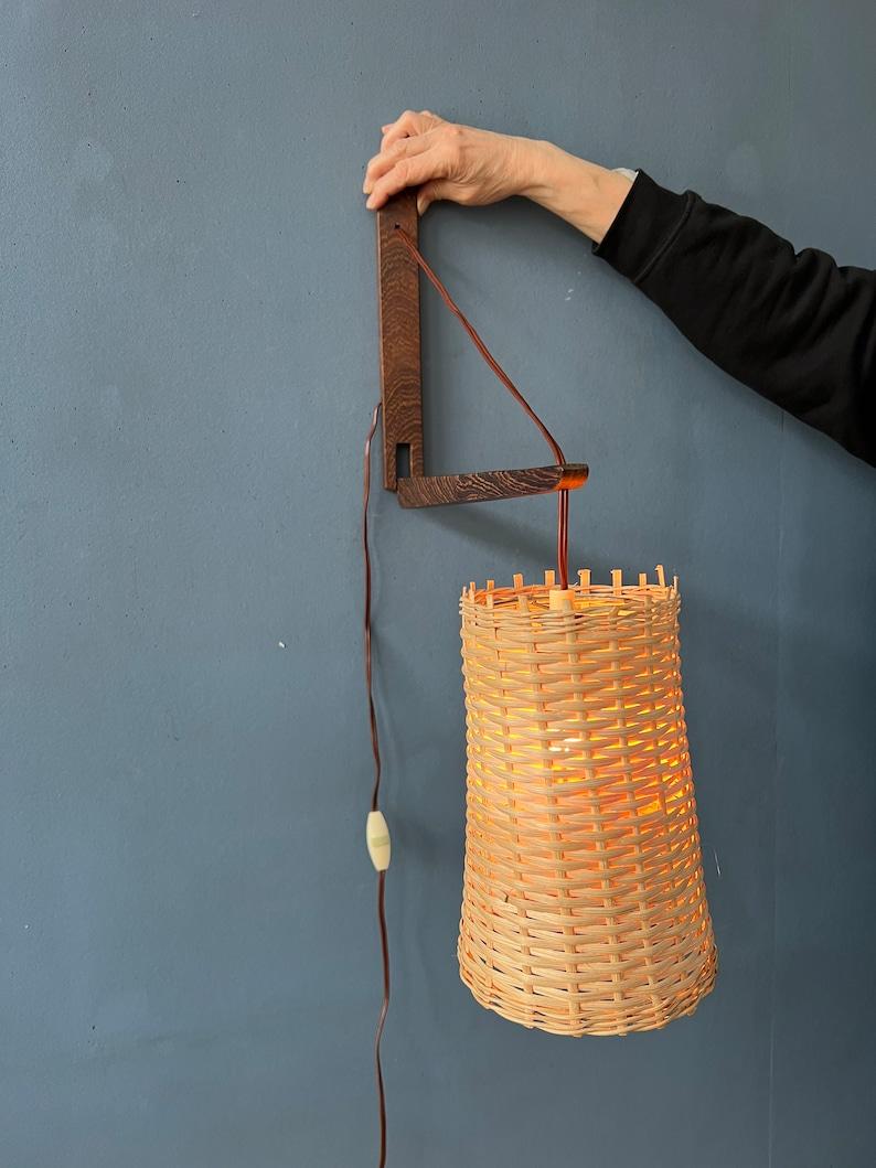 Danish mid century fishing rod teak wood wall lamp with reed shade. The position of the teak wood rod can easily be adjusted, as to hang the shade higher or lower. The lamp is simple in design and very light weight. The lamp requires an E27/26