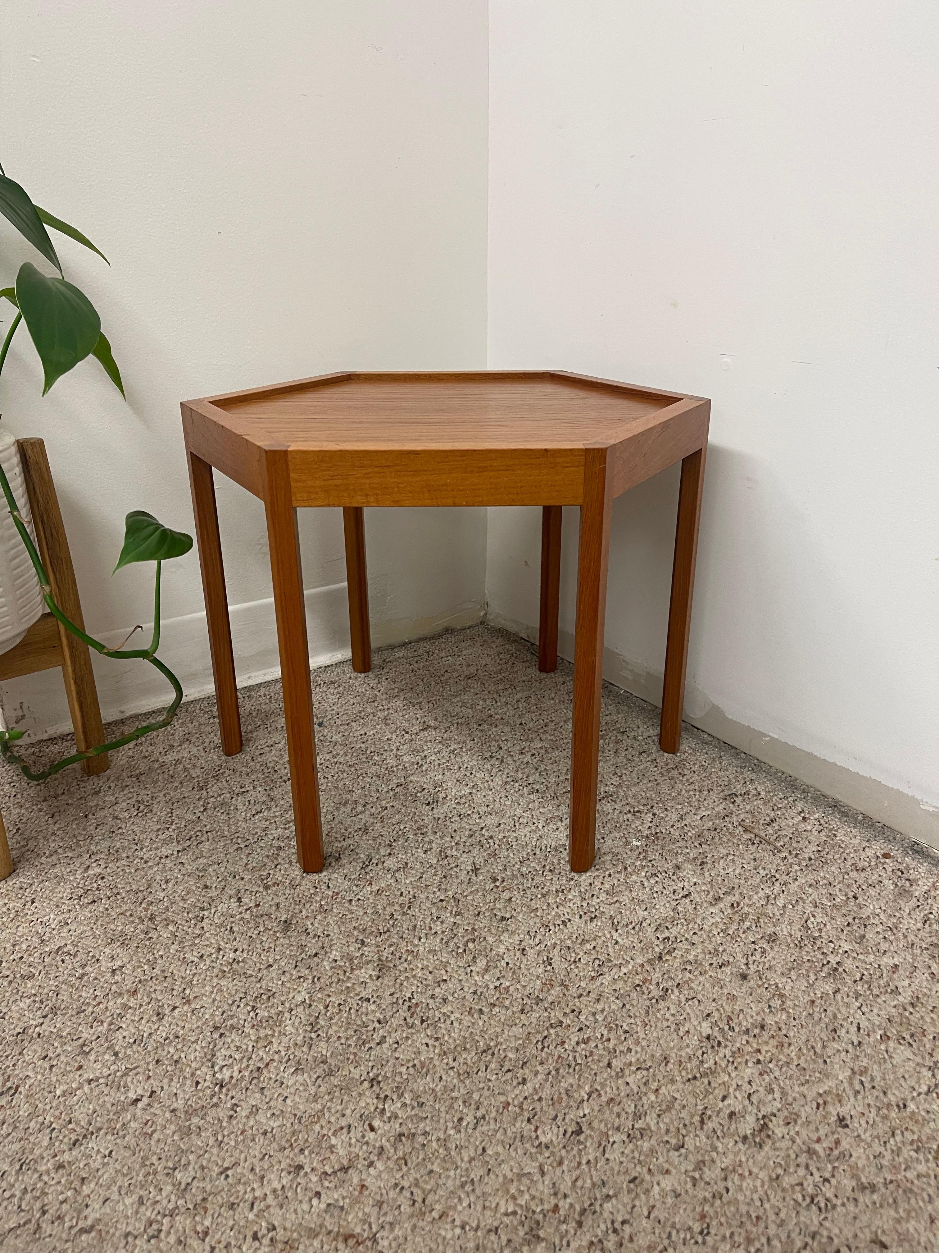 This Mid-Century Modern Danish side table, attributed to designer Hans Christian Andersen, features a striking hexagonal top crafted in warm, straight-grained teakwood. The geometric surface is framed by precisely mitered edges, forming a raised lip
