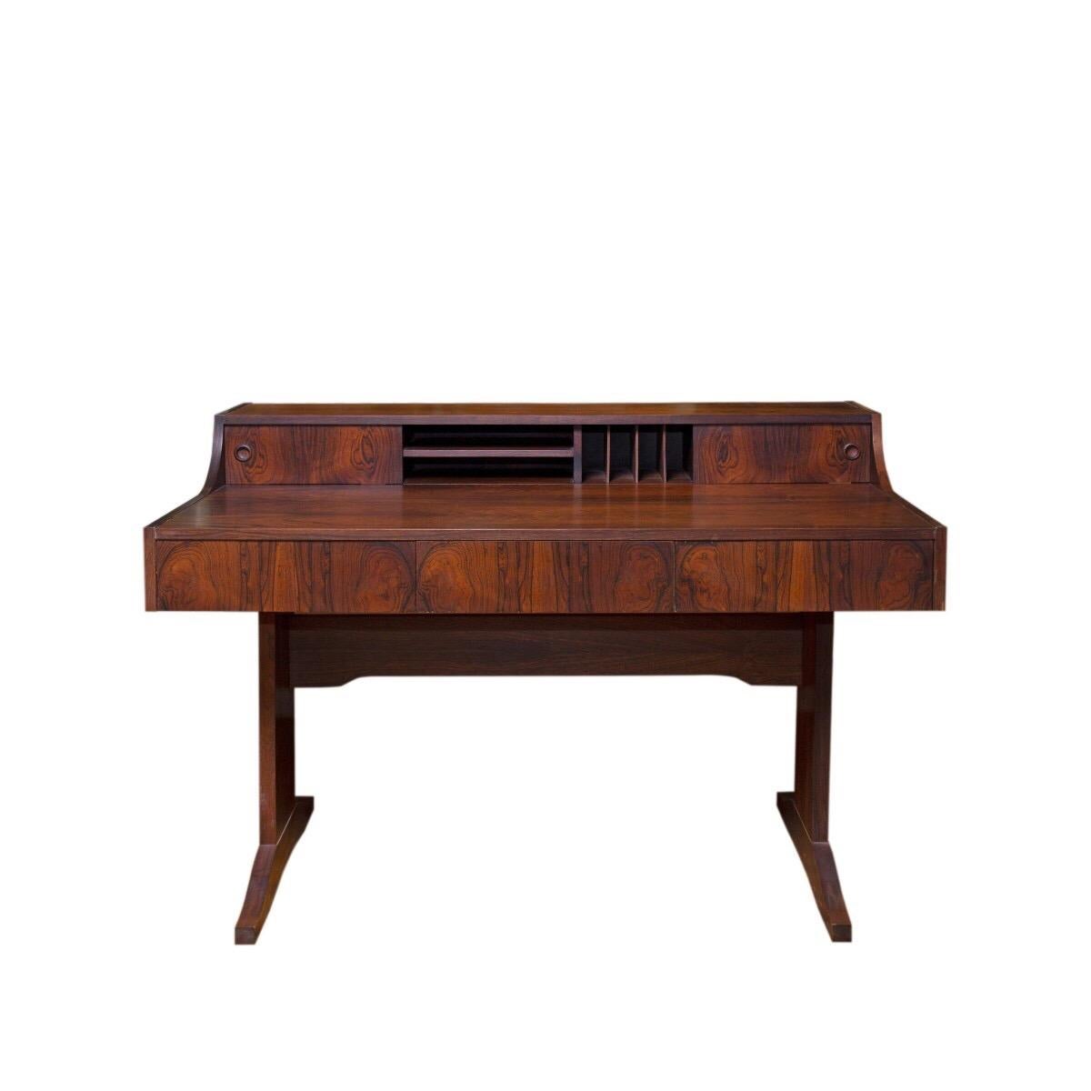 A stylish Danish trestle-base desk. Unsigned, circa 1950.

Features splayed legs, a flush front drawer and upper storage shelf with two sliding doors, two horizontal slots and four vertical letter slots. 

Made of richly grained rose