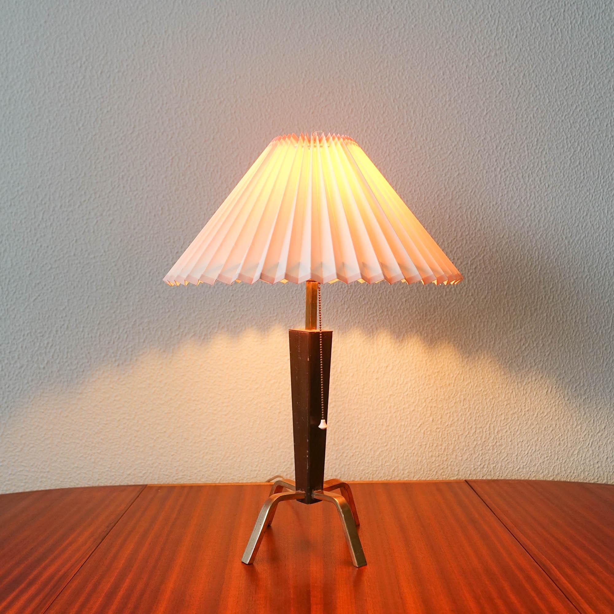 This table lamp was designed and manufactured in Denmark during the 1950's. It has a solid exotic wood body, four feet in brass and a pleated lampshade in fabric. In original and good condition.