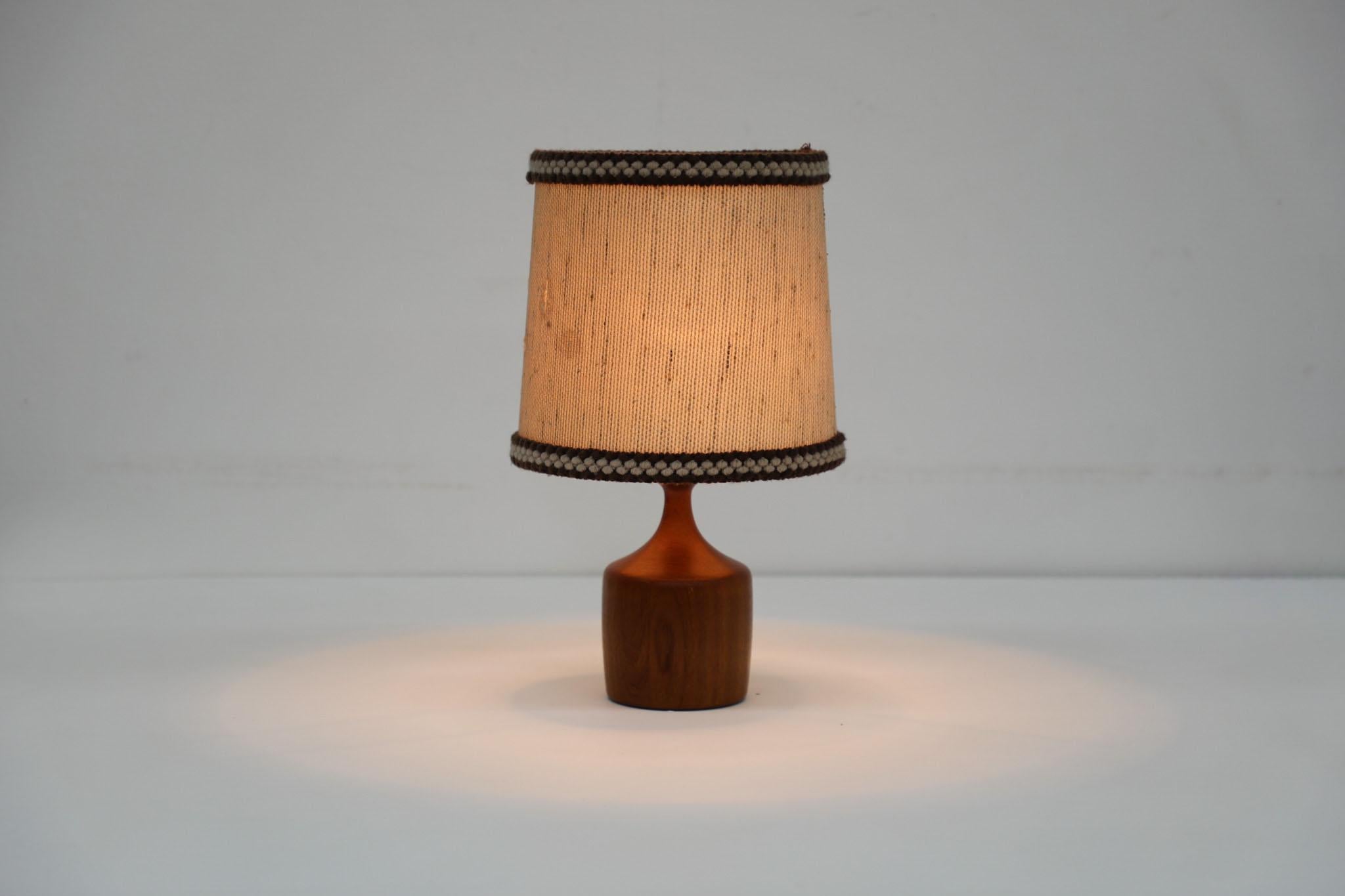 Solid turned wood table lamp with knit edged fabric shade. This vase shaped table lamp is crafted from a single piece of solid wood. In good overall condition with visible wear and spots on original shade, wear consistent with its age and use. Base