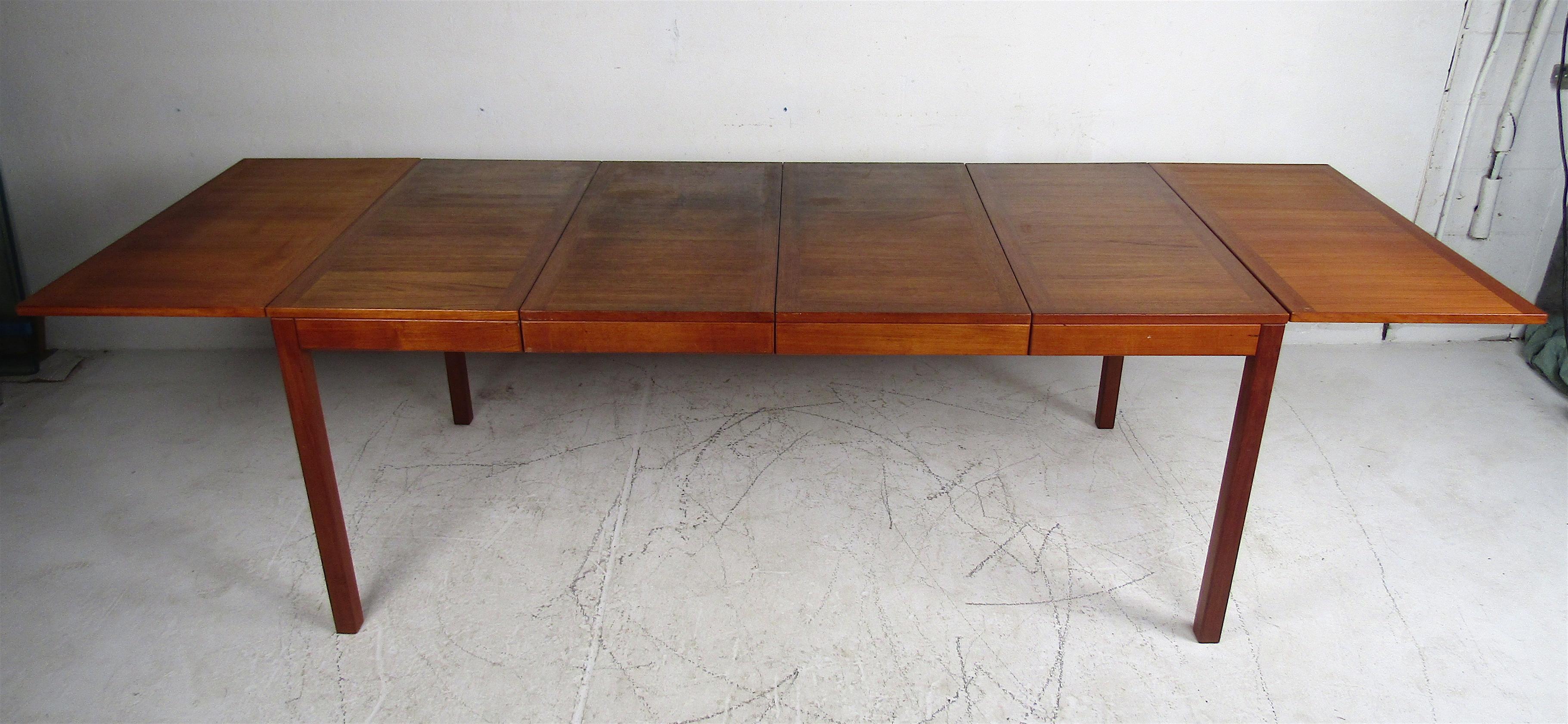 A beautiful Mid-Century Modern teak drop leaf dining table with two removable leaves ensuring convenience for additional guests. A rich vintage teak finish with the original manufacturers label underneath. A sleek design that is sure to make a