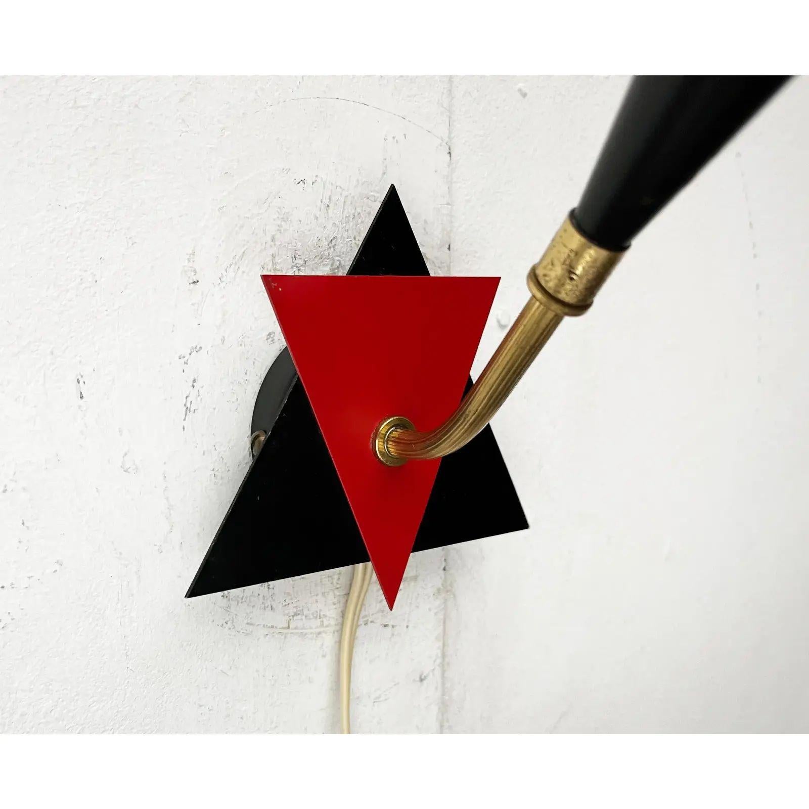 Aplique de mediados de siglo de origen danés.

El diseño impresiona por su forma y color. La base de la pared está cubierta con dos triángulos equiláteros de color rojo y negro. La toma situada en el extremo del eje acodado de latón está cerrada con