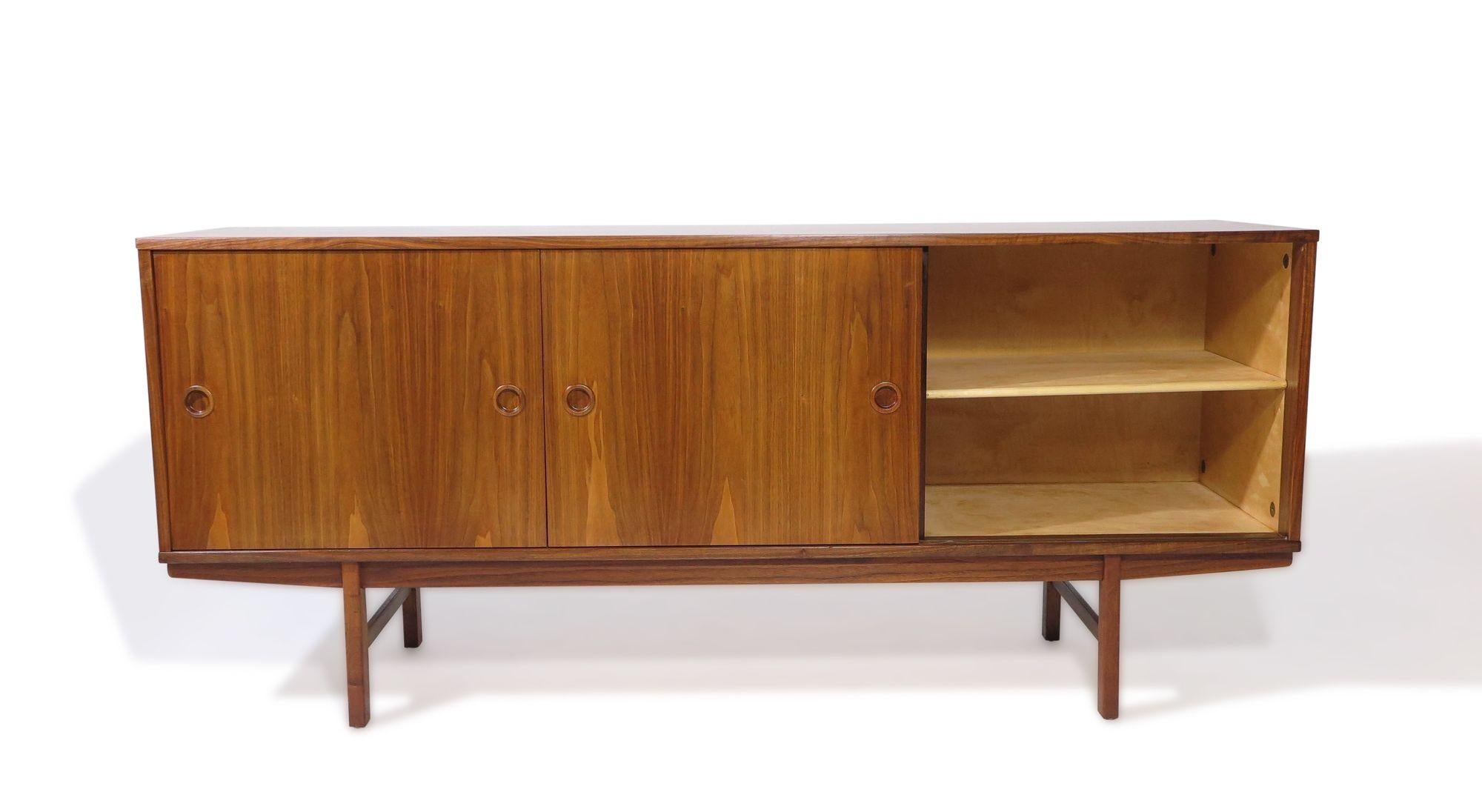 Midcentury Danish walnut credenza with sliding doors and series of five drawers in center, each with book-matched grain and recessed square pulls. The sliding doors open to reveal an interior of beech with adjustable shelves. Raised on squared legs.