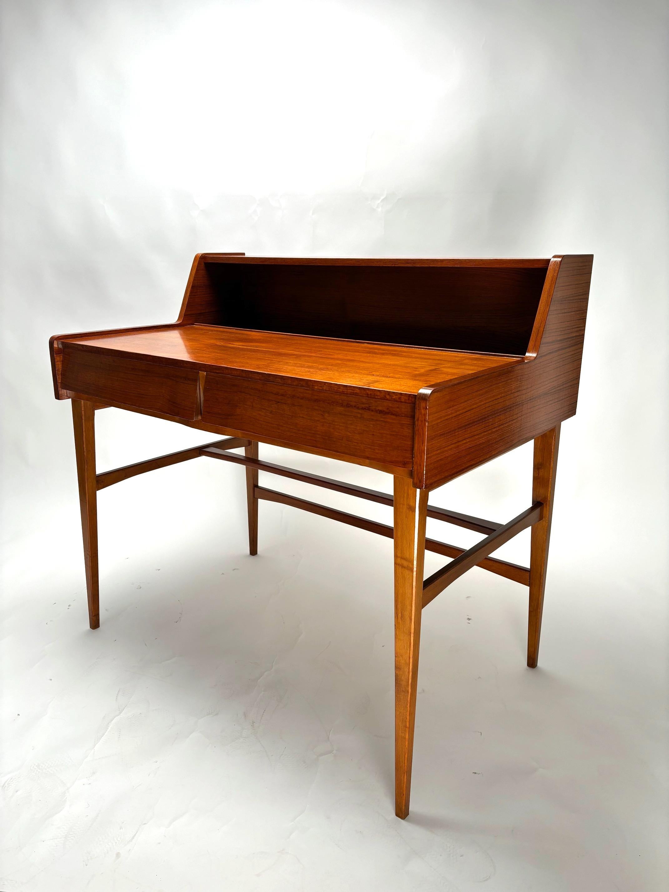 Raffinato scrittoio Mid-Century in legno di teak danese, molto comodo e versatile grazie a un comodo piano, due spaziosi cassetti frontali e una nicchia libreria posizionata all'estremità del piano. 1960s