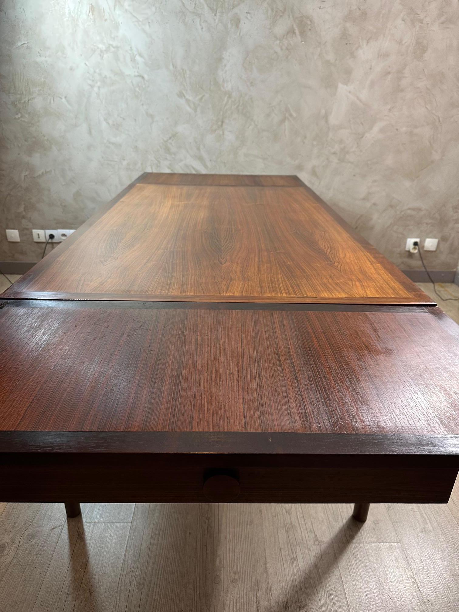 Magnifique table de salle à manger danoise des années 1950, fabriquée en bois massif, un bois précieux très recherché pour son grain profond et sa tonalité chaude.
Le plateau de la table présente un étonnant motif en bois, typique des créations