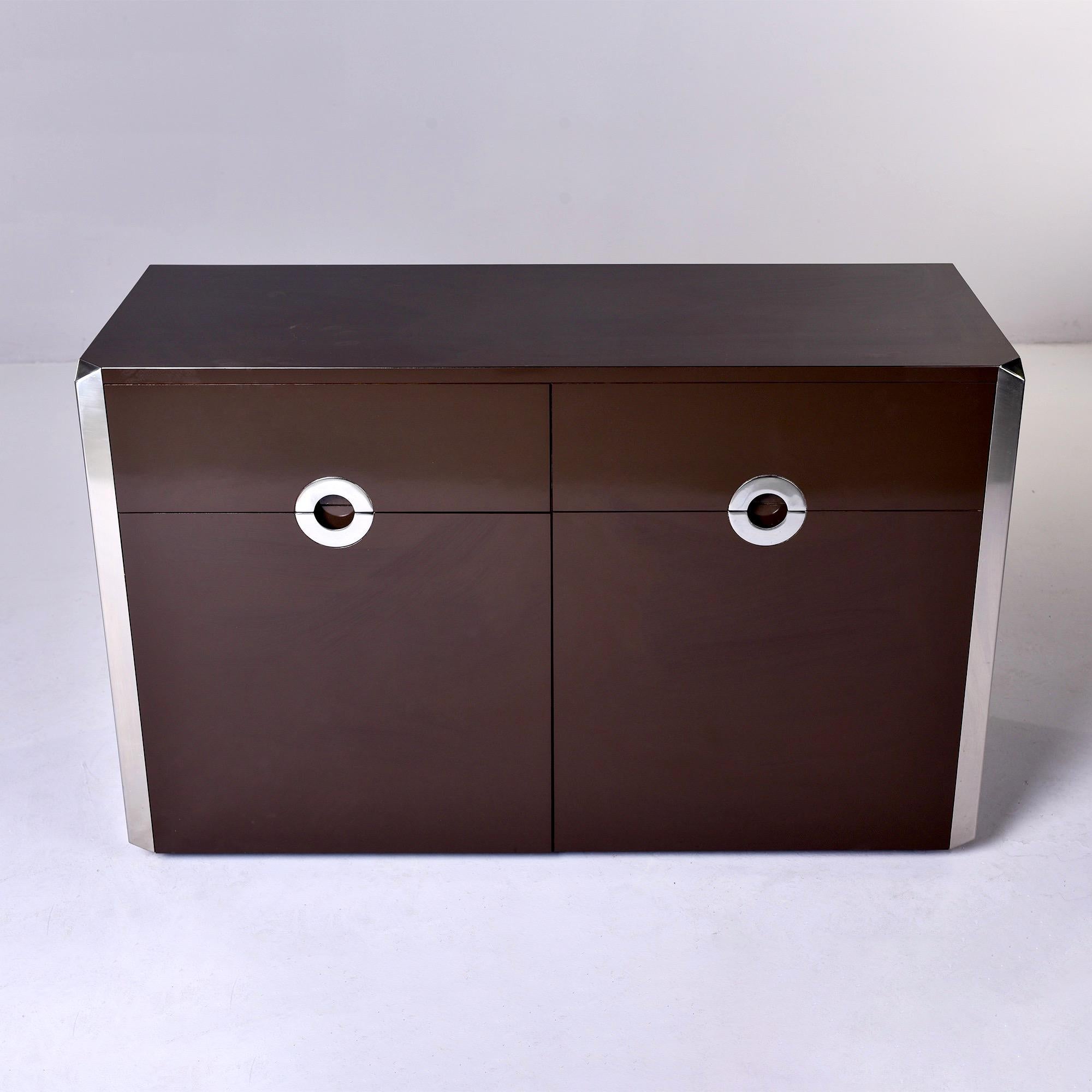 Found in Italy, this cabinet has a dark brown lacquer finish with two drawers over a two door cabinet that opens to divided storage compartment with a single internal shelf on each side. Recessed circle form chrome pulls. Unknown maker.

Very good