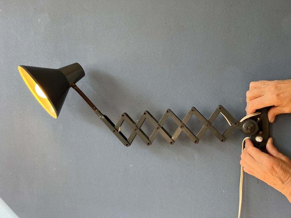 Grey mid century scissor wall lamp made out of metal. The lamp can stretch out and fold easily with the extendable scissor mechanism. The lamp itself can also move upward and downward from the wall bracket. Also the shade can be turned with its