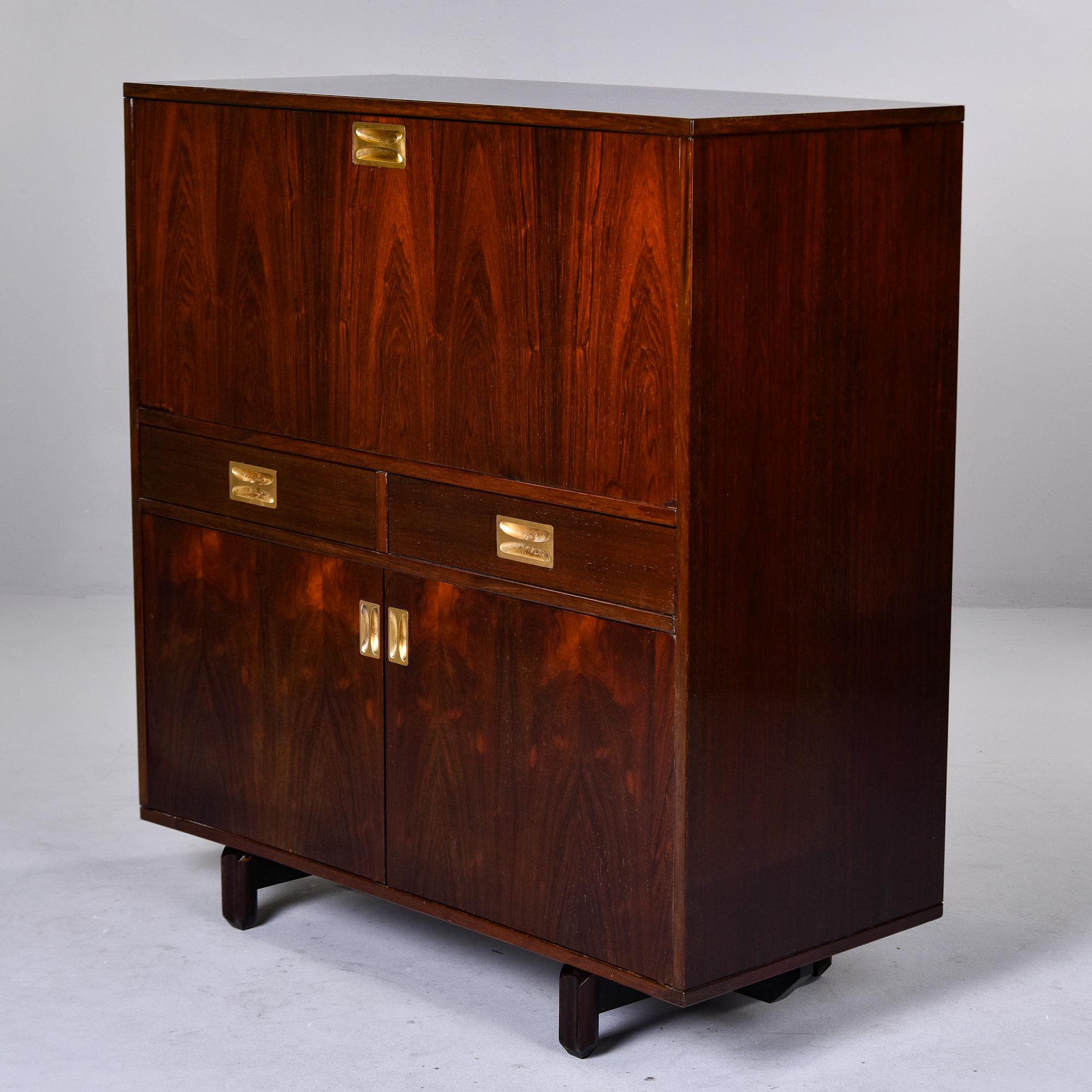 Found in France, this piece piece dates from the 1960s and can be used as a dry bar cabinet or secretary desk. Covered in dark mahogany veneer with brass hardware, this cabinet features a drop down desk or work surface with divided storage, two