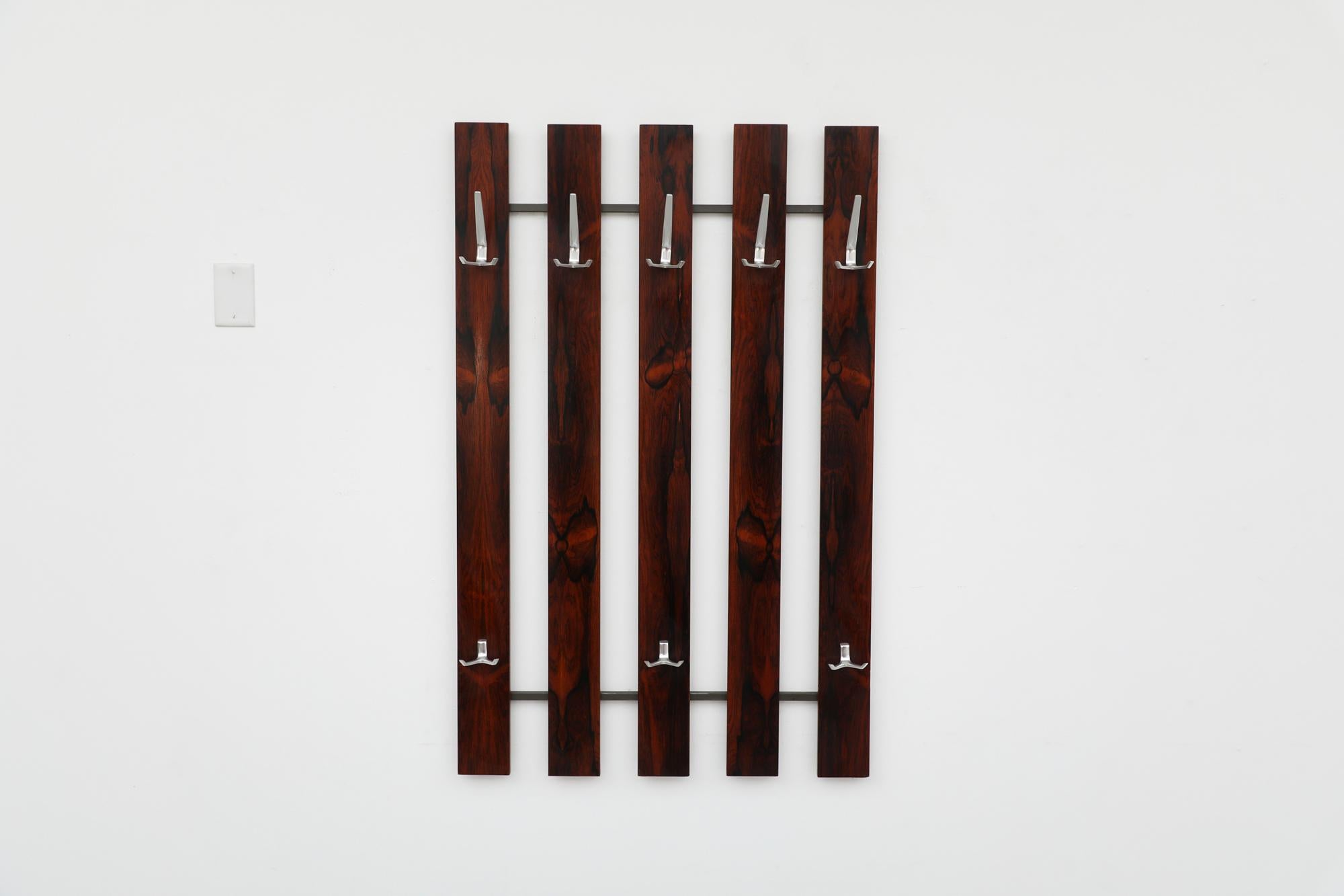 Beautiful mid-century Rosewood wall mounted coat rack with 8 cast aluminum hooks. In original condition with minimal wear and scratching. Similar coat racks also available and listed separately in various tones, also available in Wenge. Please