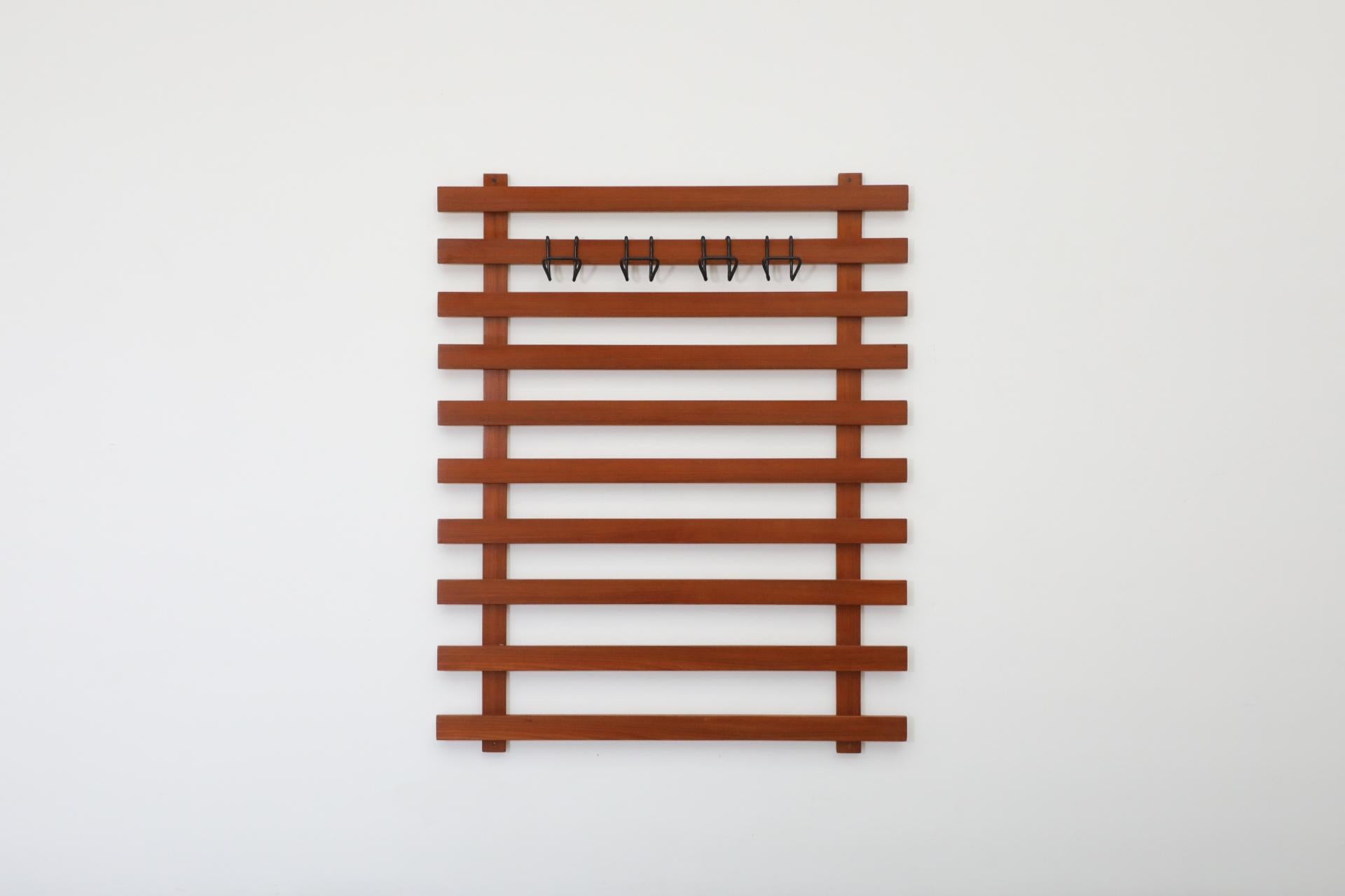 Grande appendiabiti da parete a doghe in teak con 4 grandi ganci a 's' in filo metallico curvato smaltato nero. I ganci possono essere posizionati su qualsiasi doga e contengono ciascuno un cappello, due giacche o camicie. In condizioni originali,