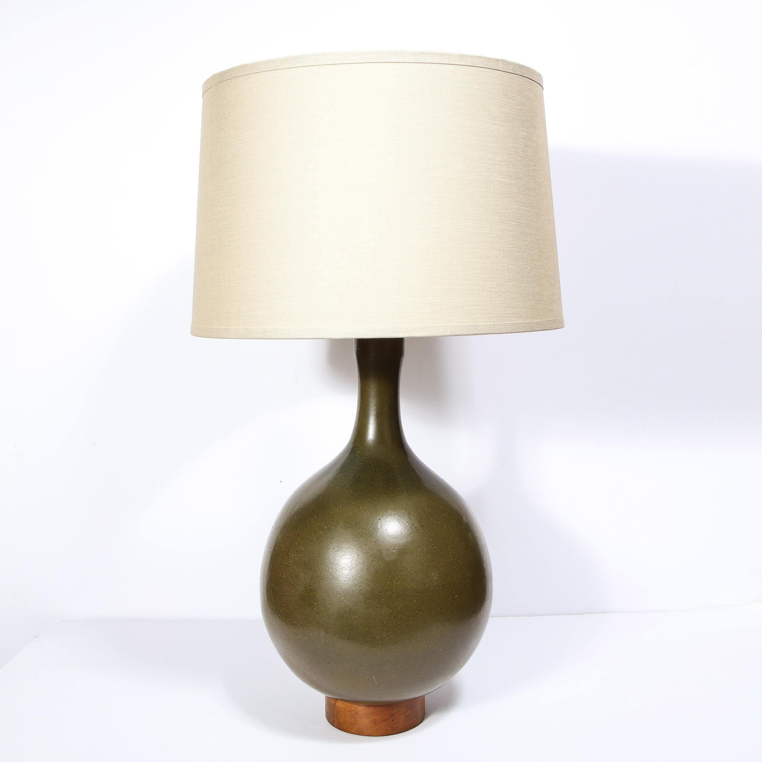 This strikingly beautiful ceramic table lamp was created by David Cressey in California, c 1960s. This wheel thrown voluminous lamp features a earthy mossy green colored glaze with a walnut rounded base in a warm brown tone. The newly rewired lamp