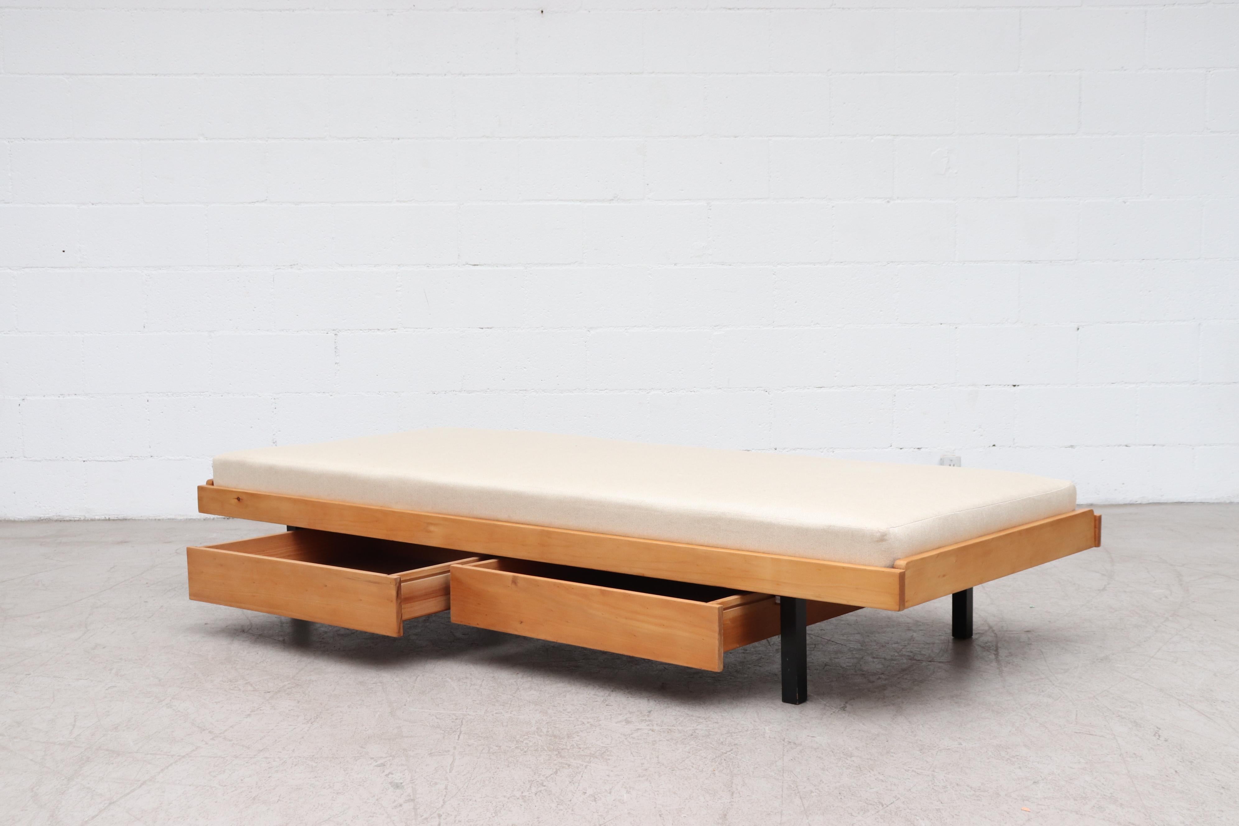 Mid-century daybed with new upholstered mattress on a lightly refinished blonde wood frame with double lower drawers and square black enameled metal legs. In original condition with some frame wear consistent with age and use.
