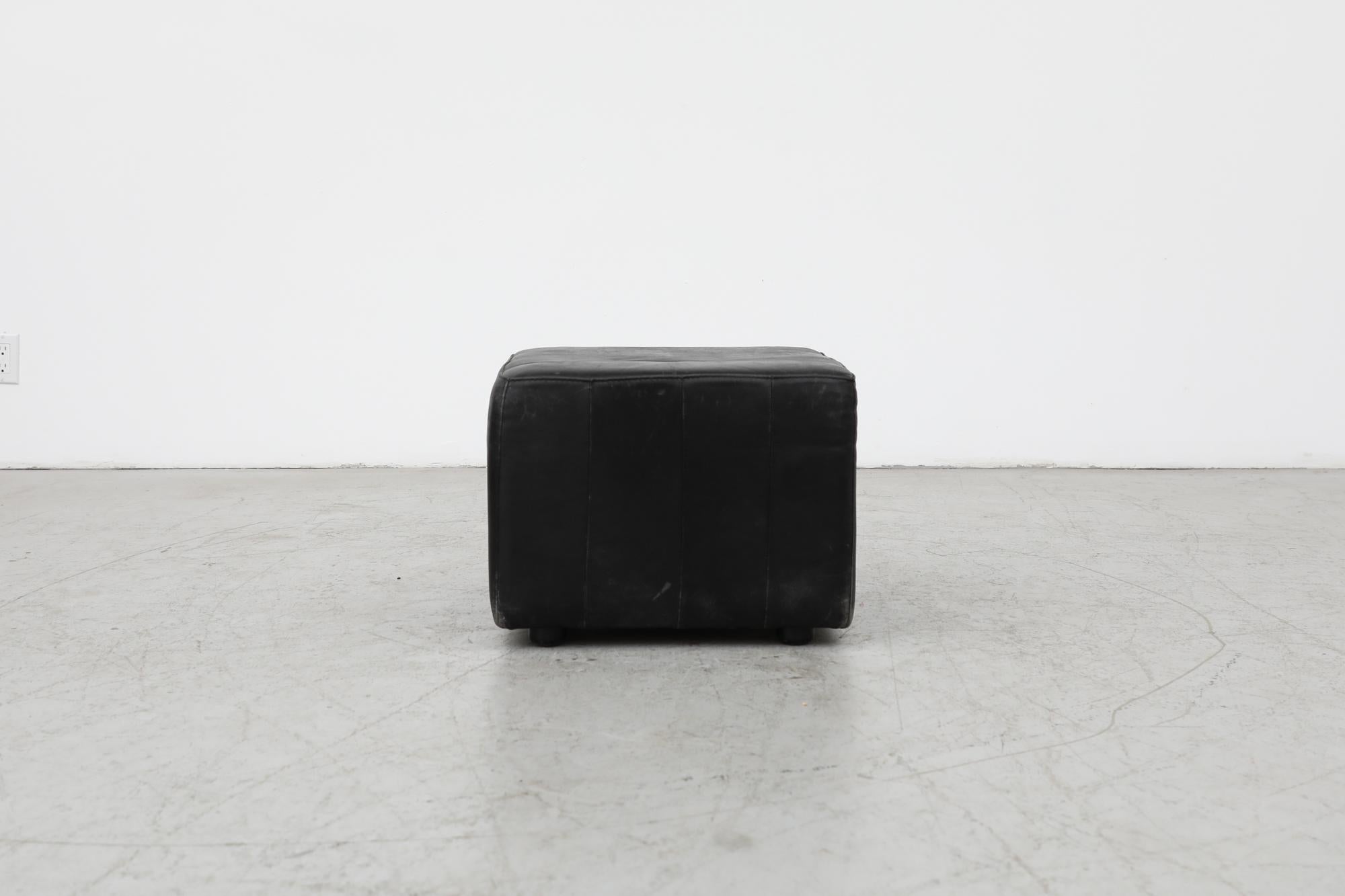 Mid-Century De Sede style black leather cube ottoman. In original condition with visible wear, including scratching, consistent with its age and use.