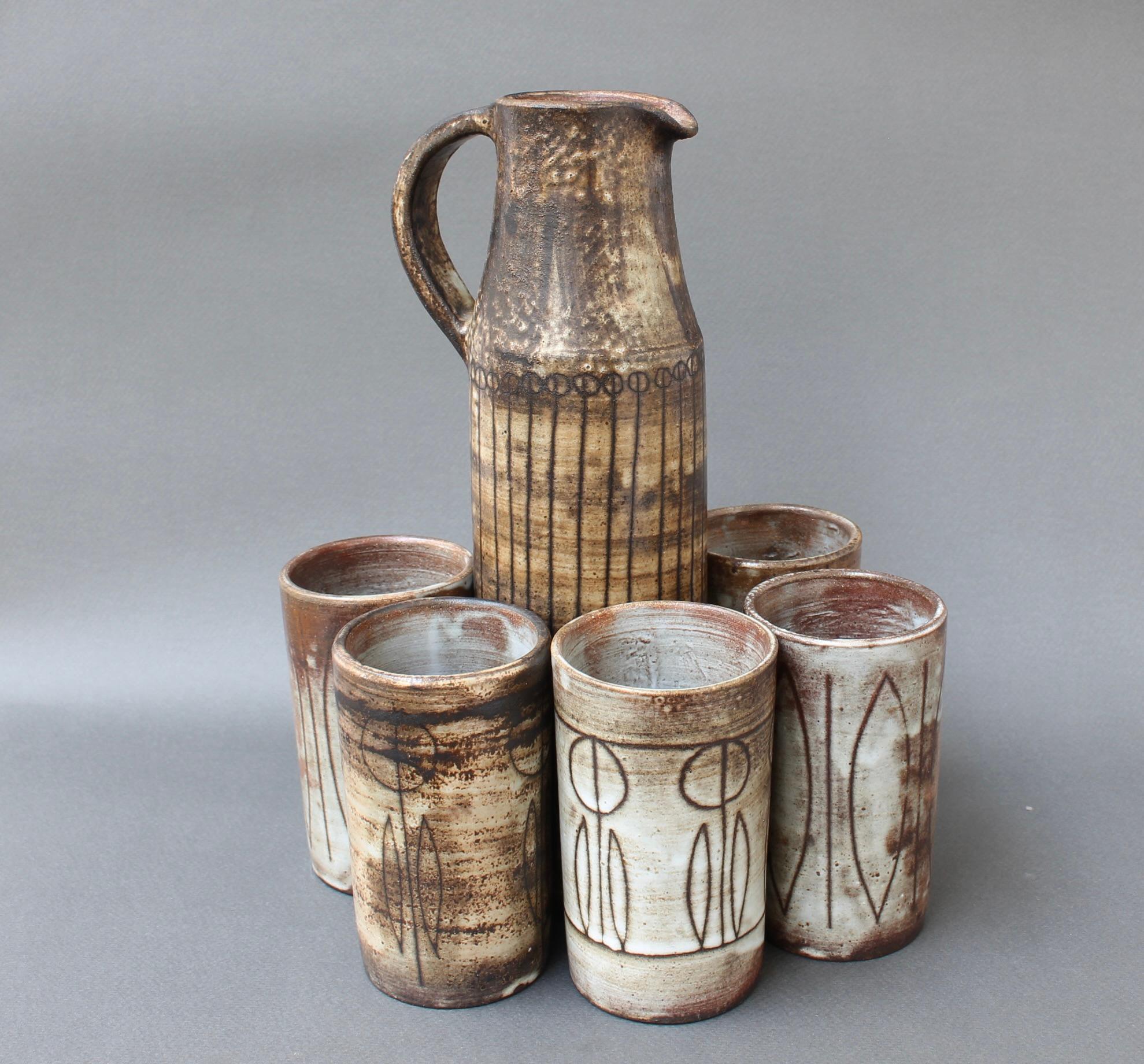 Vintage decorative ceramic drink set by Jacques Pouchain / Atelier Dieulefit (circa 1960s). Classic cylindrical vase/pitcher with sensuously curved handle in Pouchain's signature cloudy glaze style with earth tone hues. The cups are beautiful in