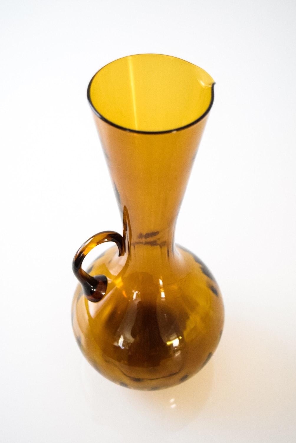 This vintage midcentury decorative glass pitcher is a beautiful deep amber and features a sleek and elegant Mid-Century Modern design with a lovely profile. It can be used as a small water pitcher, decorative pitcher or vase.

Dimensions
Height: