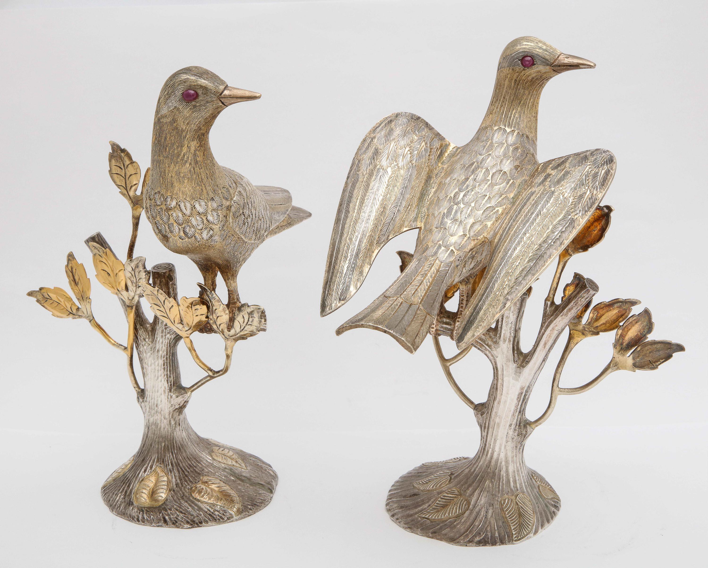 Midcentury decorative pair of sterling silver table birds with real ruby eyes, Mexico, circa 1950s, Tane - maker. Each bird is perched on a tree branch. Both sterling silver figures are parcel-gilt. The measurements are as follows: The bird with its