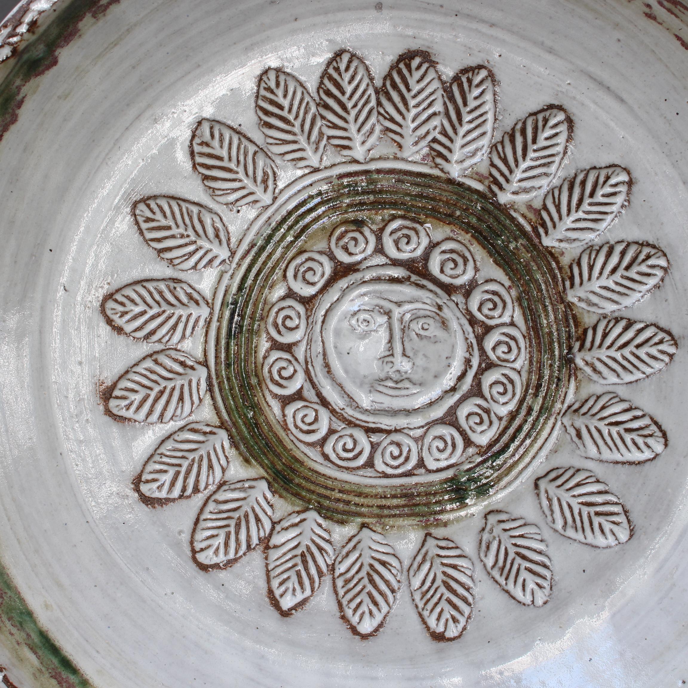 Mid-century decorative platter (circa 1960s) by Albert Thiry. A milky-white glaze graces both the exterior and the hollow centre. The interior has small tracts of green and earthy clay which surround a central medallion with face and flower motif.