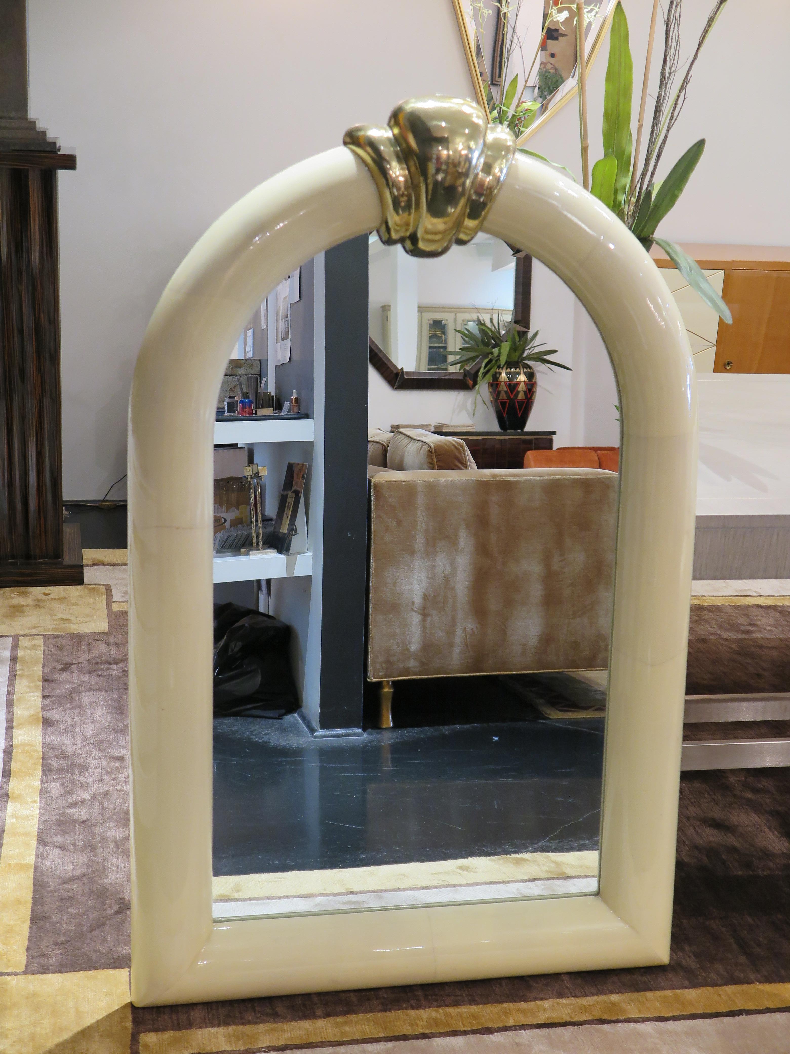 Mid-century mirror with demi-lune frame in parchment (goatskin) with a high gloss finish. Large brass scalloped ornamentation on top. This pieces is in its original condition.