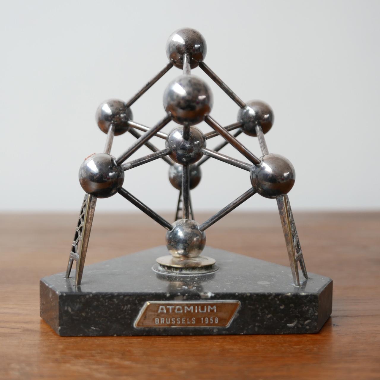 A small desk top model of the Atomium building in Brussels. 

Marble base, metal model. 

Belgium, c1960s. 

Some small nicks to the marble base, wear commensurate with age. 

Dated plaque to base. 

Location: London Gallery.