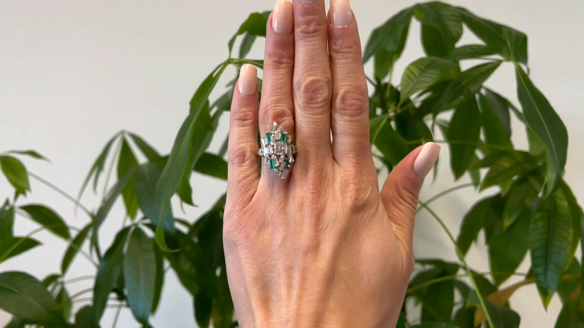 One Mid Century Diamond and Emerald Platinum Cocktail Ring. Featuring one emerald cut diamond weighing approximately 0.45 carat, graded F color, VS2 clarity. Accented by four step cut emeralds with a total weight of approximately 0.50 carat, and 21