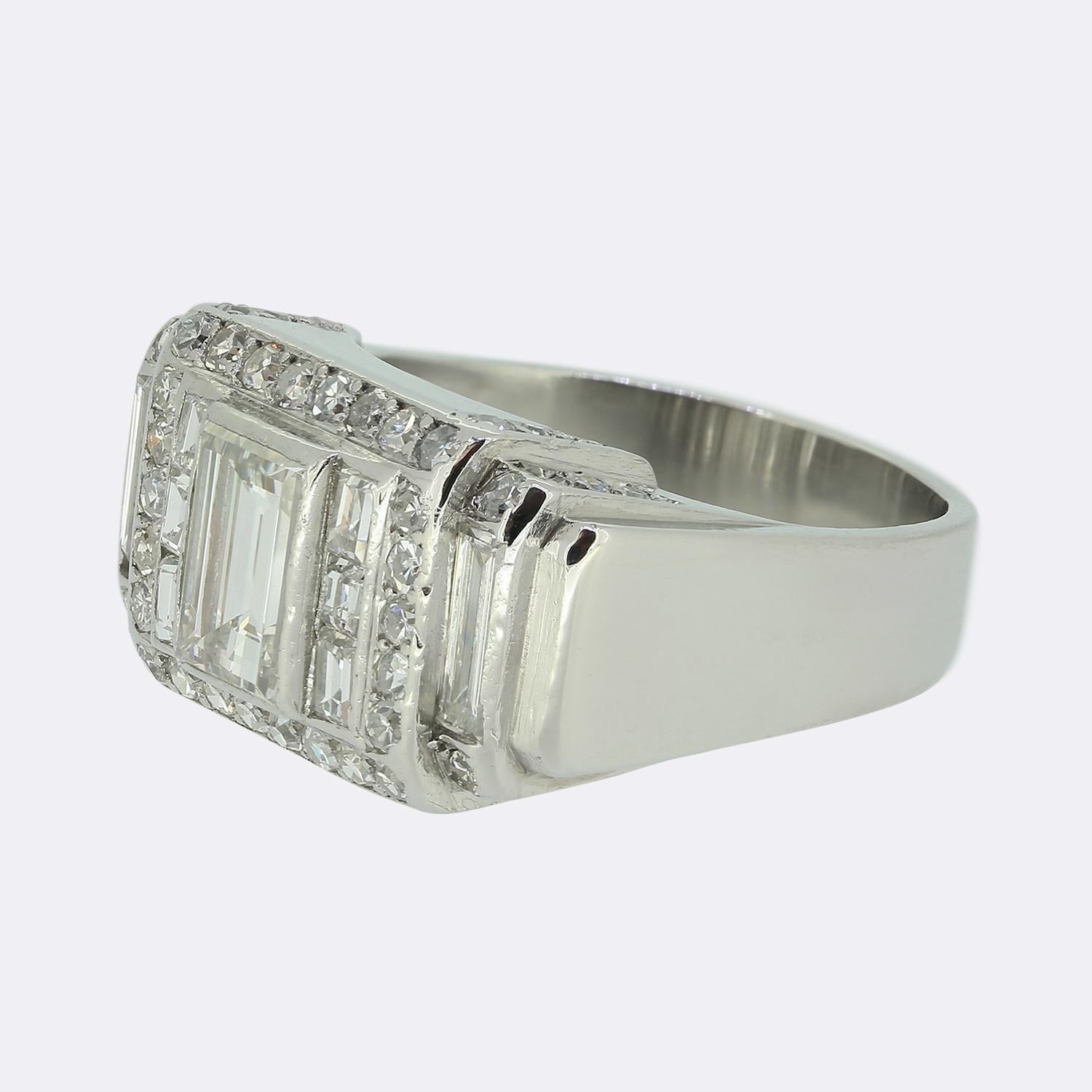 Qui abbiamo un anello a grappolo con diamanti meravigliosamente lavorato, risalente alla metà del XX secolo. Il centro del quadrante presenta un importante diamante bianco con taglio a baguette, affiancato da un canale singolo su entrambi i lati con