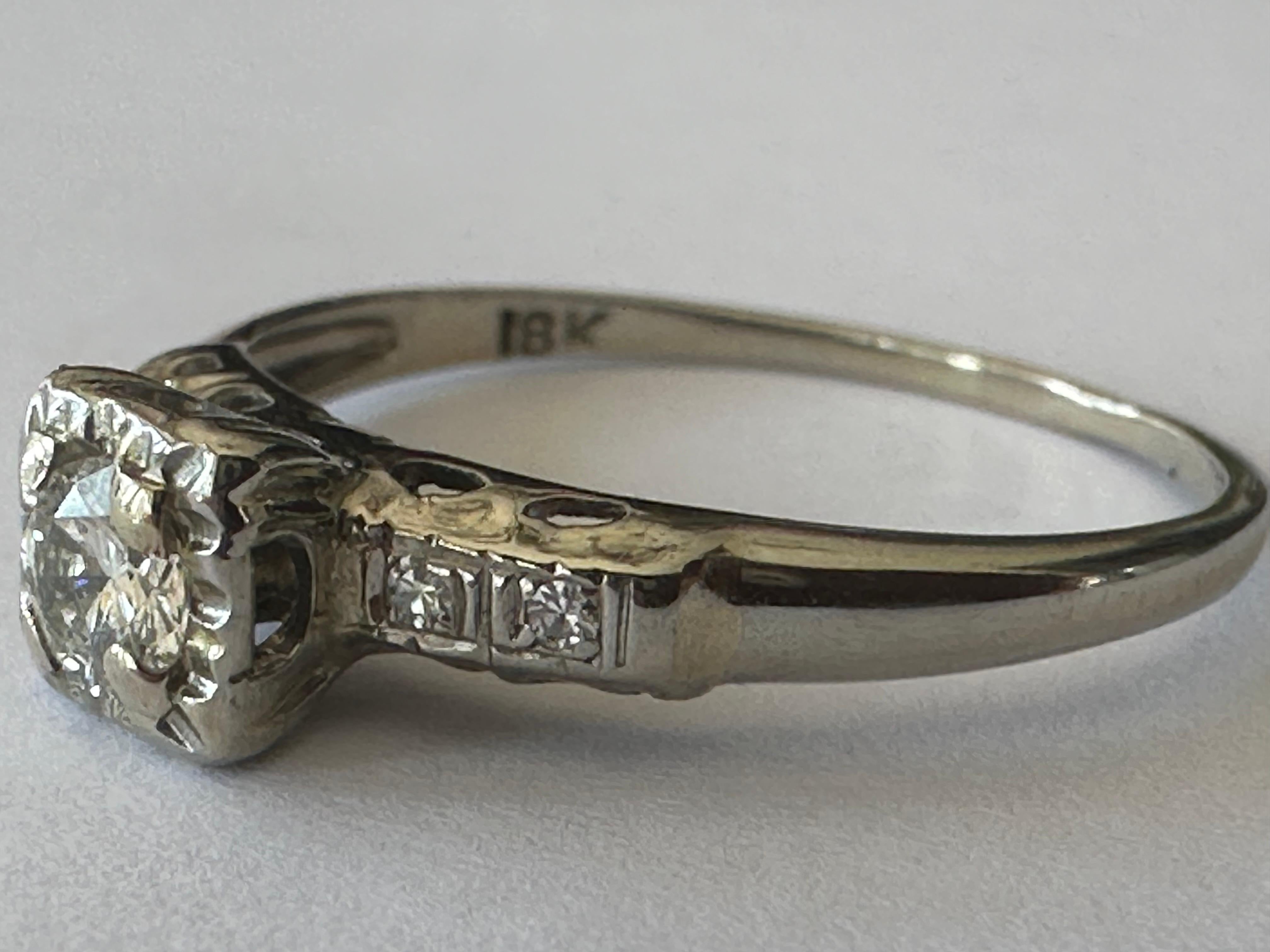 Ein Diamant im alten europäischen Schliff mit einem Gewicht von ca. 0,17 Karat, Farbe H, Reinheit SI1, leuchtet hell zwischen vier Diamanten im Einzelschliff, zwei auf jeder Schulter. Fassung aus 18 Karat Weißgold. Um 1950er Jahre. 
