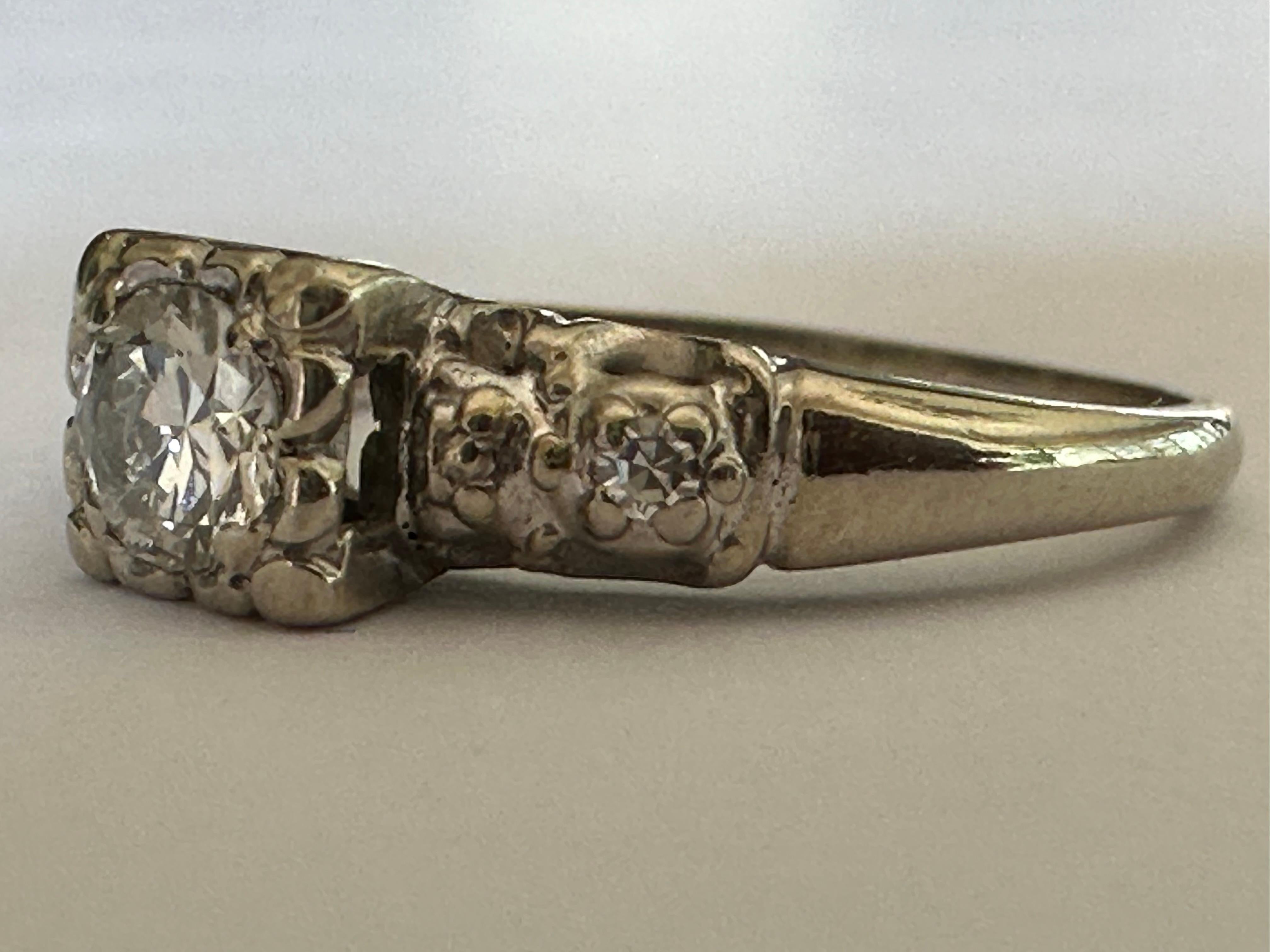 An Old European-cut diamond center stone measuring approximately 0.30 carat, F color VS clarity, shines in between finely engraved shoulders dotted with two tiny single cut diamonds. Set in 14K white gold. 
Maker's mark indicates it was most likely