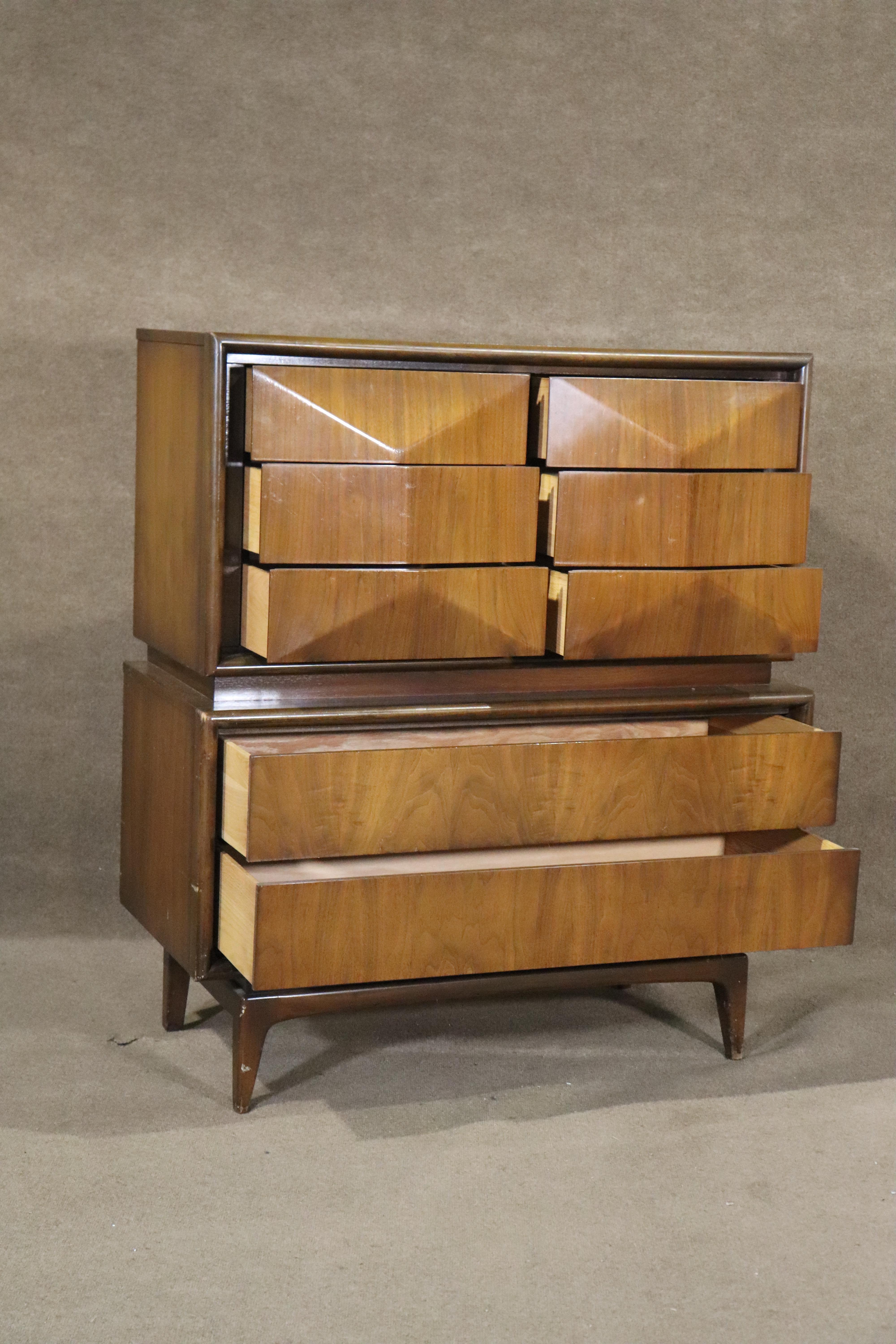 Commode haute moderne du milieu du siècle fabriquée en Amérique par United. Avec leurs tiroirs emblématiques en forme de diamant et leur grain de noyer chaleureux. Huit tiroirs au total pour le rangement de la chambre à coucher.
Veuillez confirmer