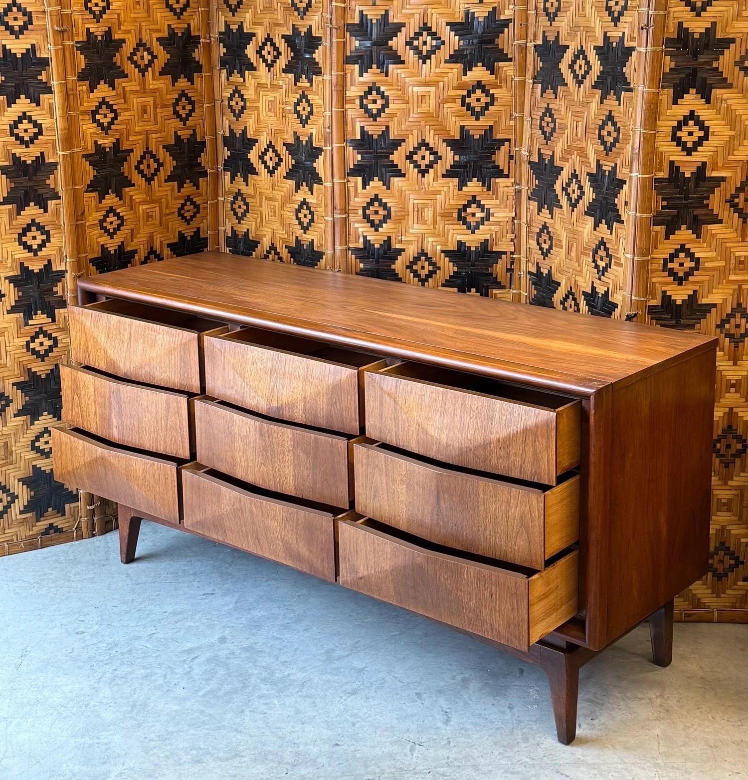 Comò di metà secolo prodotto da United Furniture. Questo pezzo fa parte della collezione Diamond Front. Il nome è giusto per i suoi cassetti anteriori intagliati in modo geometrico che creano un motivo a forma di diamante. Dispone di nove spaziosi