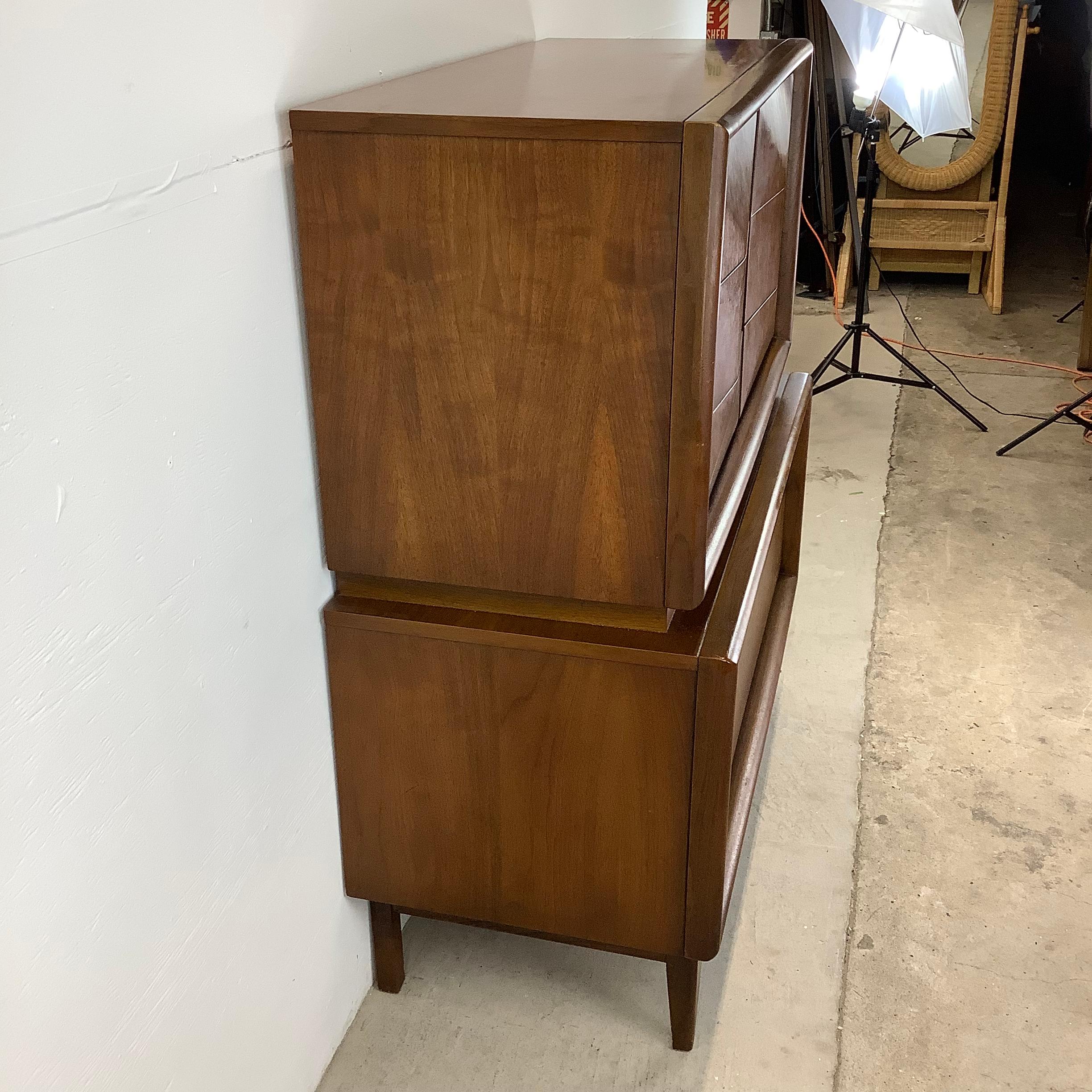 Elevate your living space with this mid-century walnut highboy from United Furniture, a sought after manufacturer of vintage modern design. This tall eight drawer dresser, with its streamlined silhouette and rich walnut finish, embodies the
