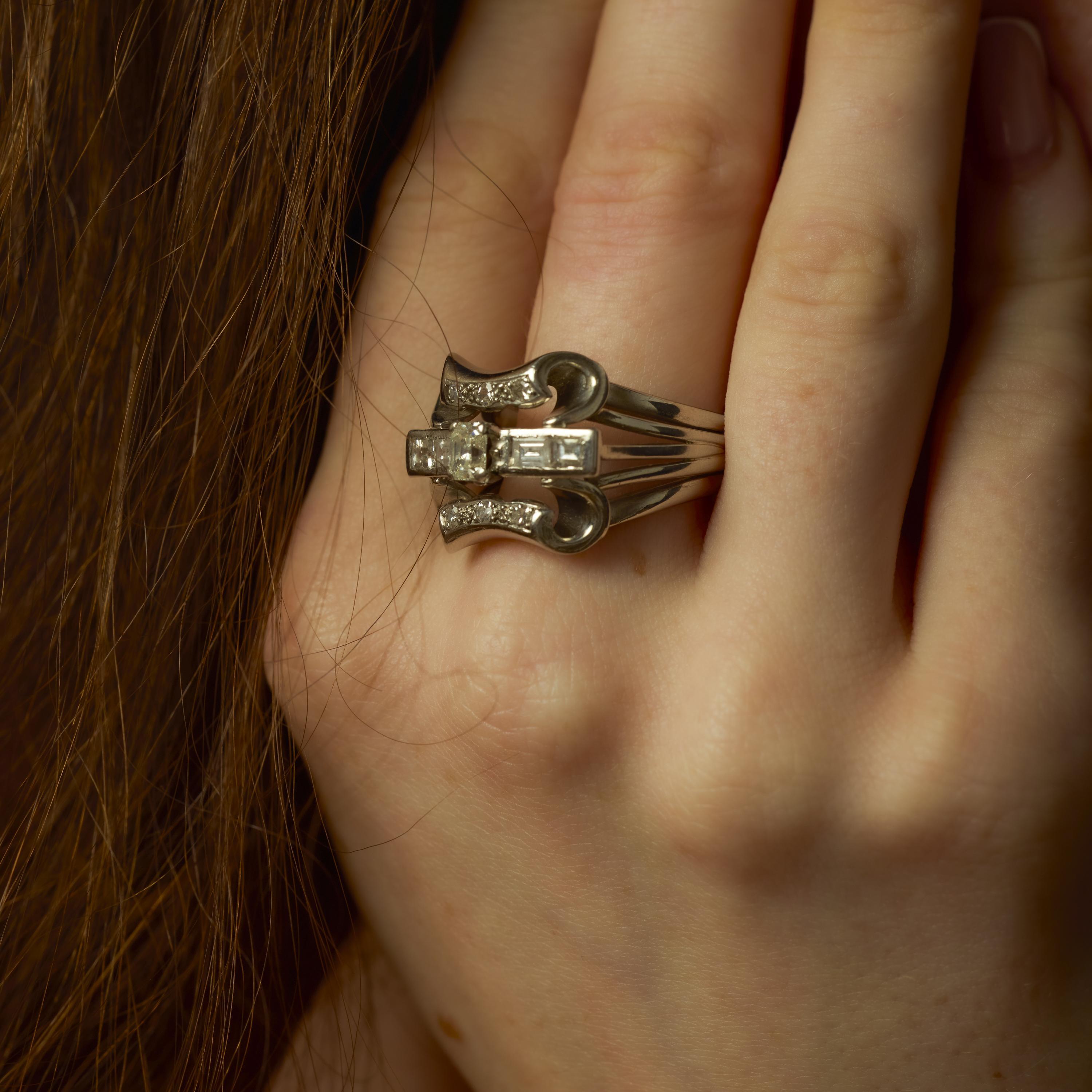 Este anillo de platino de mediados de siglo se centra en un nítido diamante talla Asscher de 0,50 quilates, apreciado por sus facetas escalonadas y su claridad VS1. Alrededor del centro hay una combinación de cuatro diamantes de talla baguette y