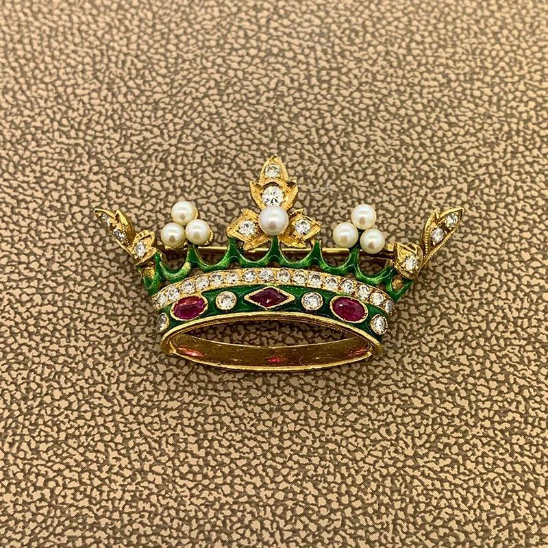 Une broche chic et élégante des années 1960 représentant une couronne royale. Parsemée de diamants ronds taillés en brillant, de rubis rouges vifs, de perles naturelles et finie avec de l'émail vert peint à la main, cette broche donne une touche