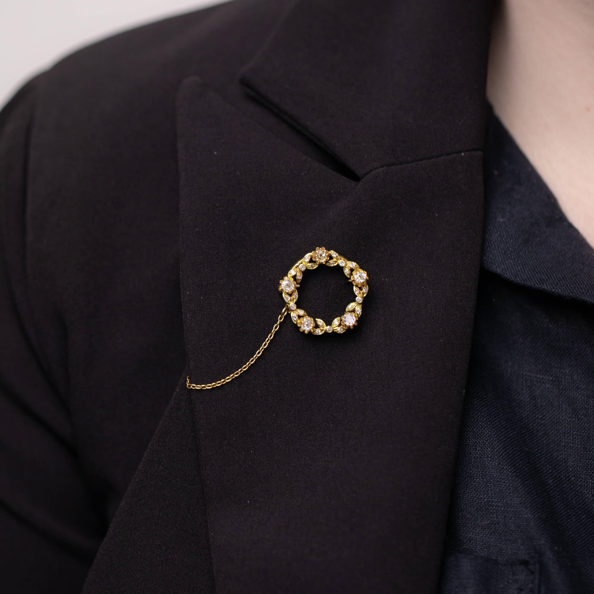 A beautiful Mid-Century circular brooch featuring a old mine cut diamonds in scalloped claw settings with a garland of diamond set leaves. Secured with a pin and roller clasp. Fitted with a safety chain with pin.

Diamonds: Five natural old mine