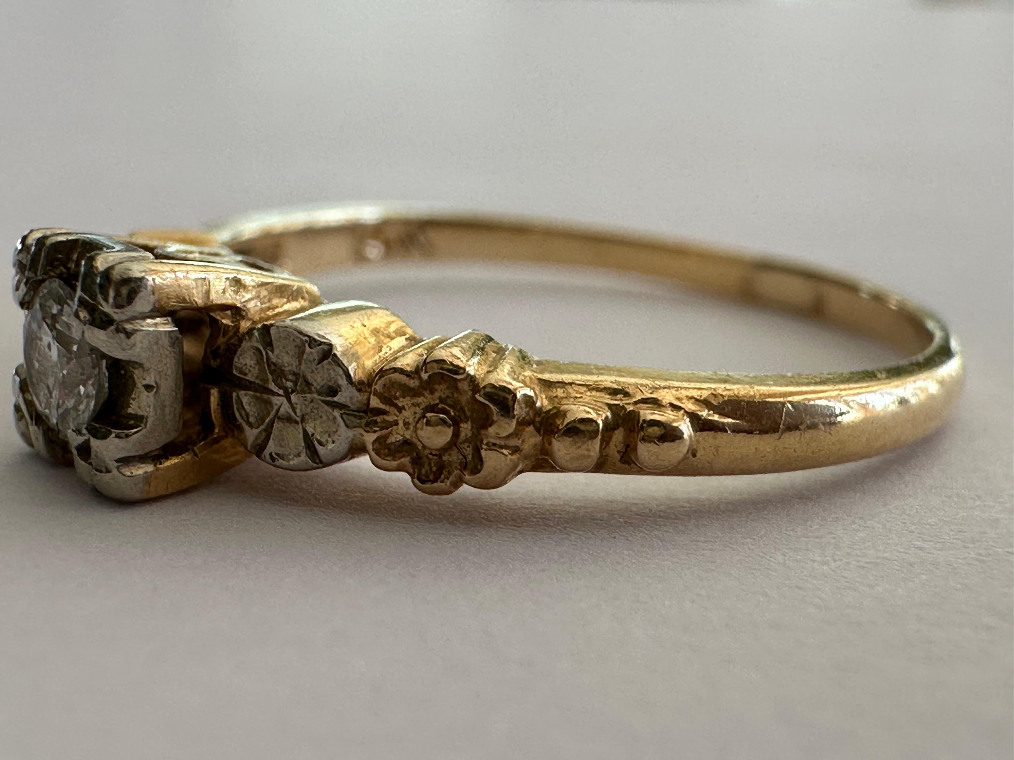 Un diamante talla vieja europea centra este anillo solitario de mediados de siglo de aproximadamente 0,10 quilates, color G claridad SI2, acentuado por flores grabadas a mano a cada lado engastadas en oro blanco y amarillo de 14 quilates bicolor.  
