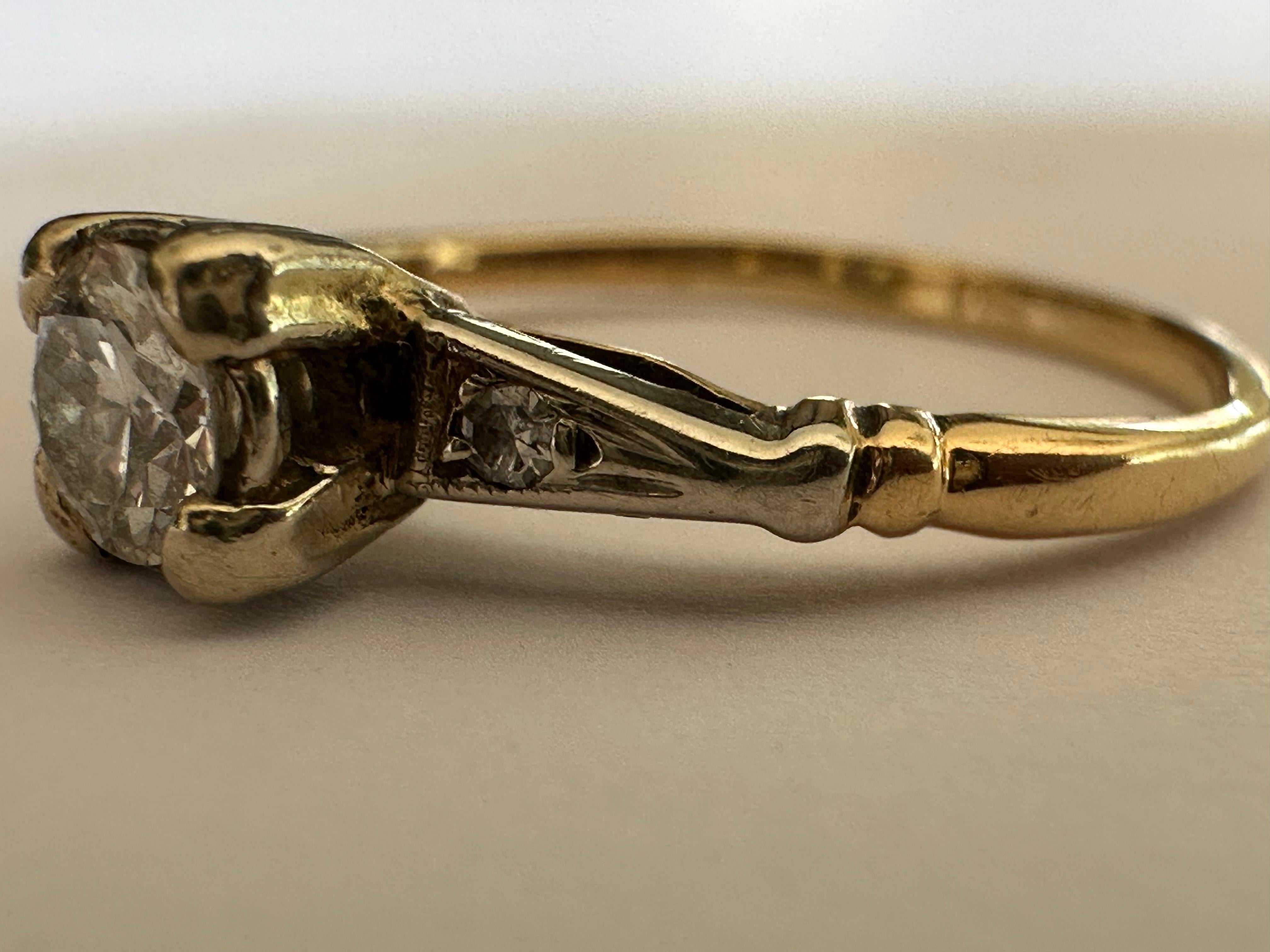 Un diamant de taille européenne ancienne mesurant environ 0,25 carat, de couleur F et de pureté VS, est au centre de cette bague du milieu du siècle, rehaussée de deux diamants de taille simple. Sertie en or jaune 14 carats. 