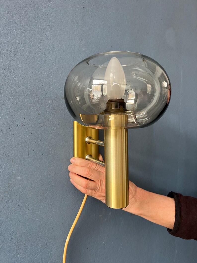 Mid century glass wall sconce with brass frame by Dijkstra. The glass is very clear and has an opening on top. The lamp requires one E27/26 lightbulb and currently has an EU-plug.

Additional information:
Materials: Metal, plastic
Period: